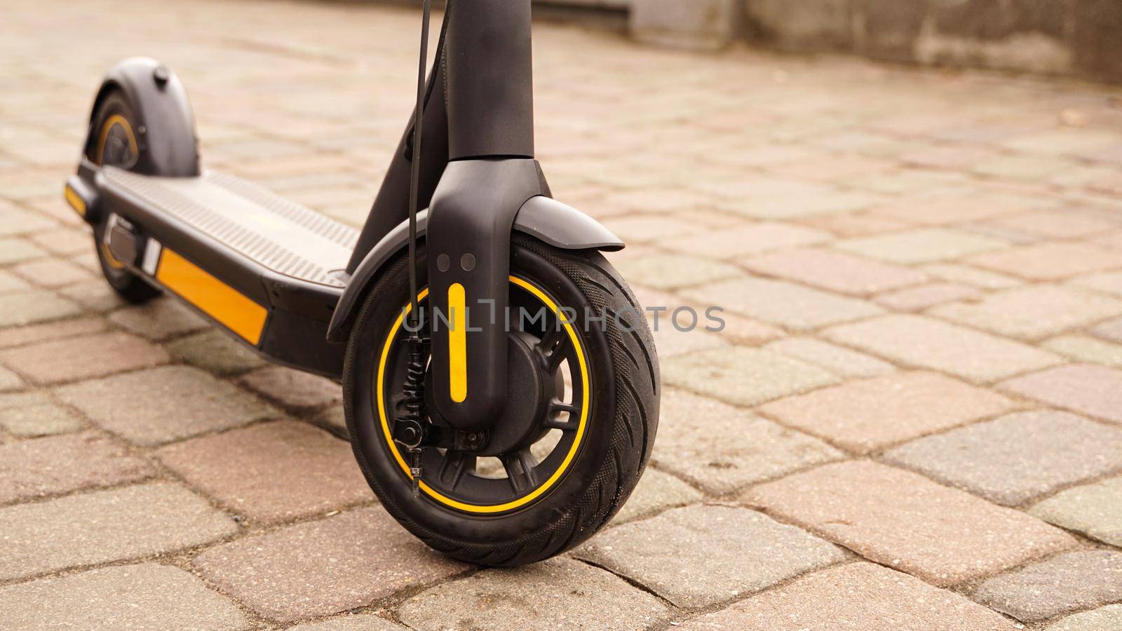 A close-up of the front wheel of an electric scooter against a tile backdrop. by natali_brill