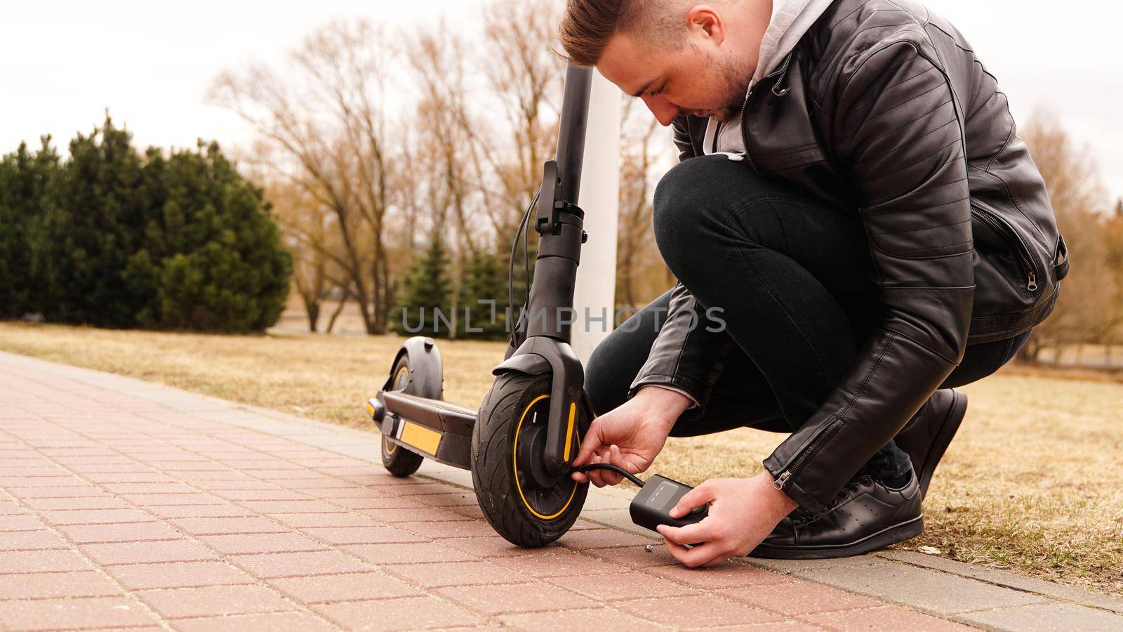 A man pumps air into the wheel of an electric scooter using a special device. Photo outside. A flat tire while driving.