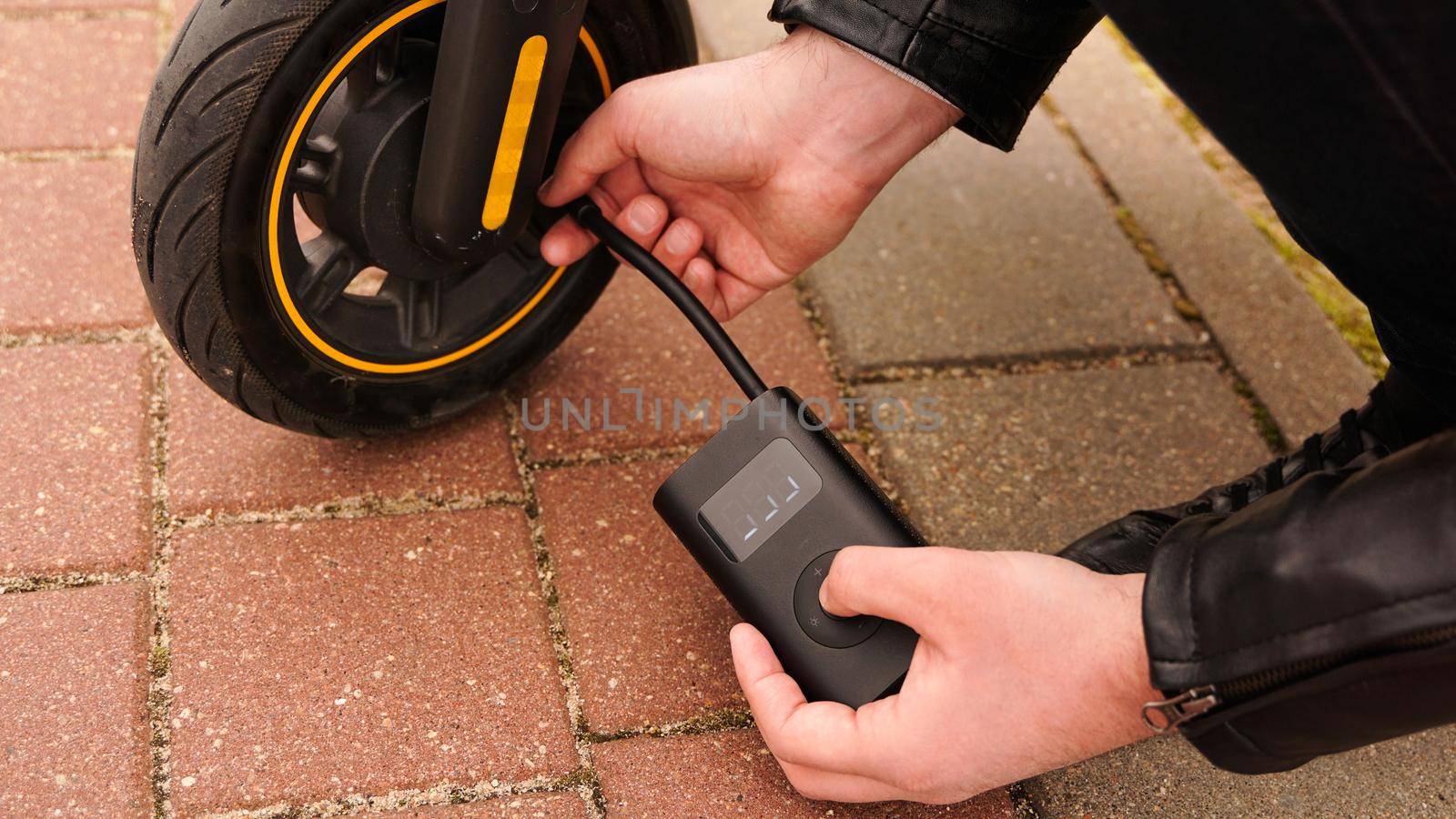 A man pumps air into the wheel of an electric scooter using a special device. Photo outside. A flat tire while driving.