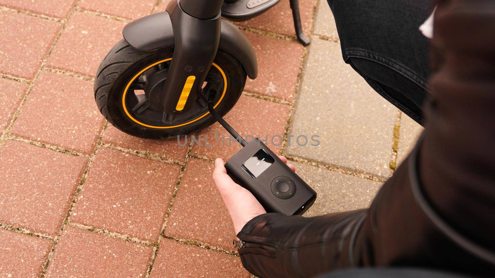 A man pumps air into the wheel of an electric scooter using a special device. Photo outside. A flat tire while driving.