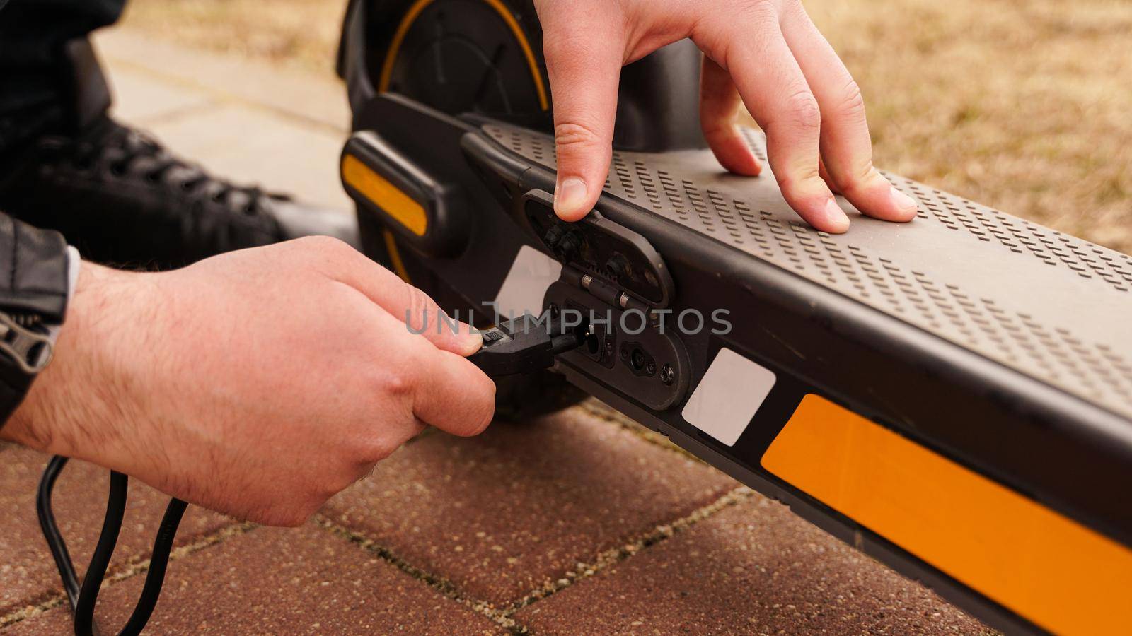 Man is charging his electrical scooter with charger on special parking. Closeup photoshoot