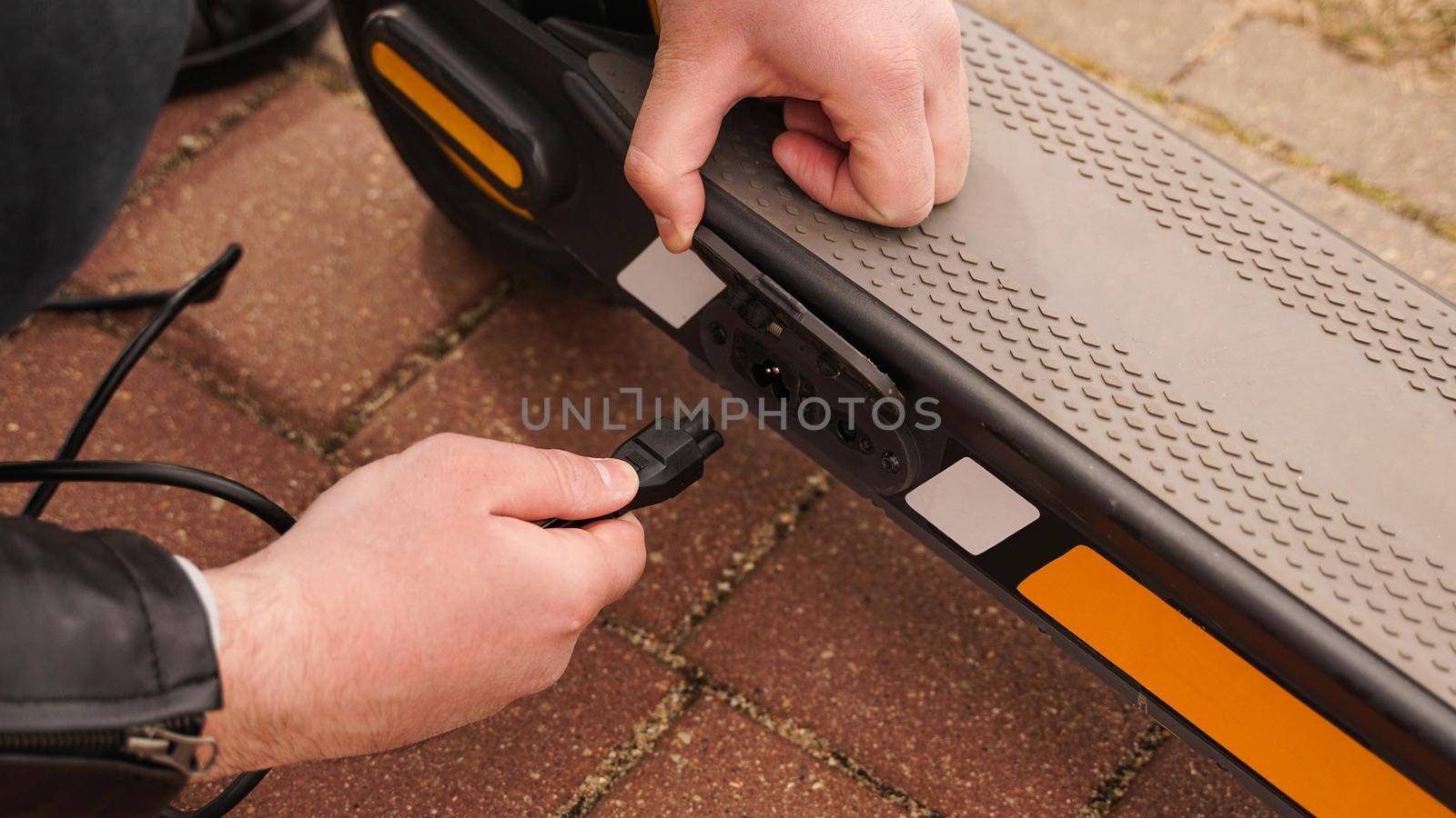 Man is charging his electrical scooter with charger on special parking. Closeup photoshoot