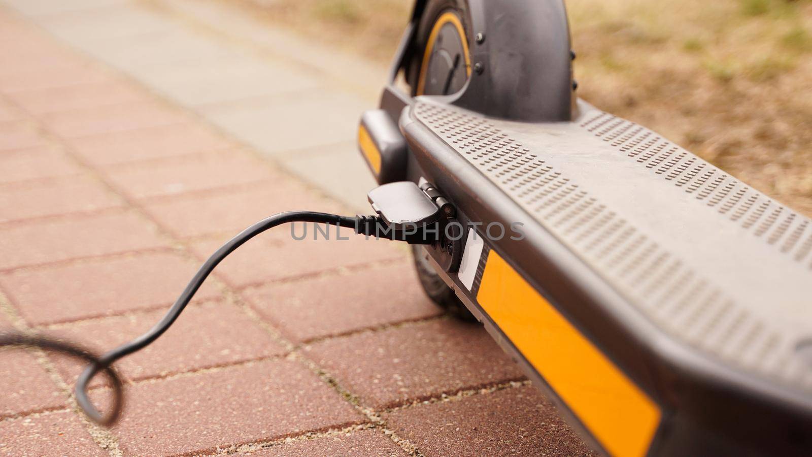 The electric scooter is charging outdoors. The wire runs into the camera. by natali_brill