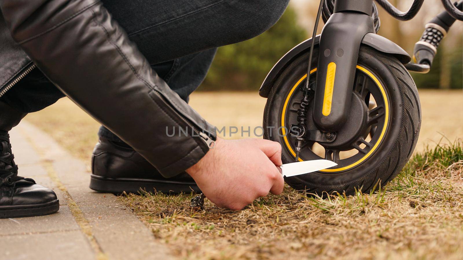 A man's hand is cutting the tire of an electric scooter with a knife. Crime concept.