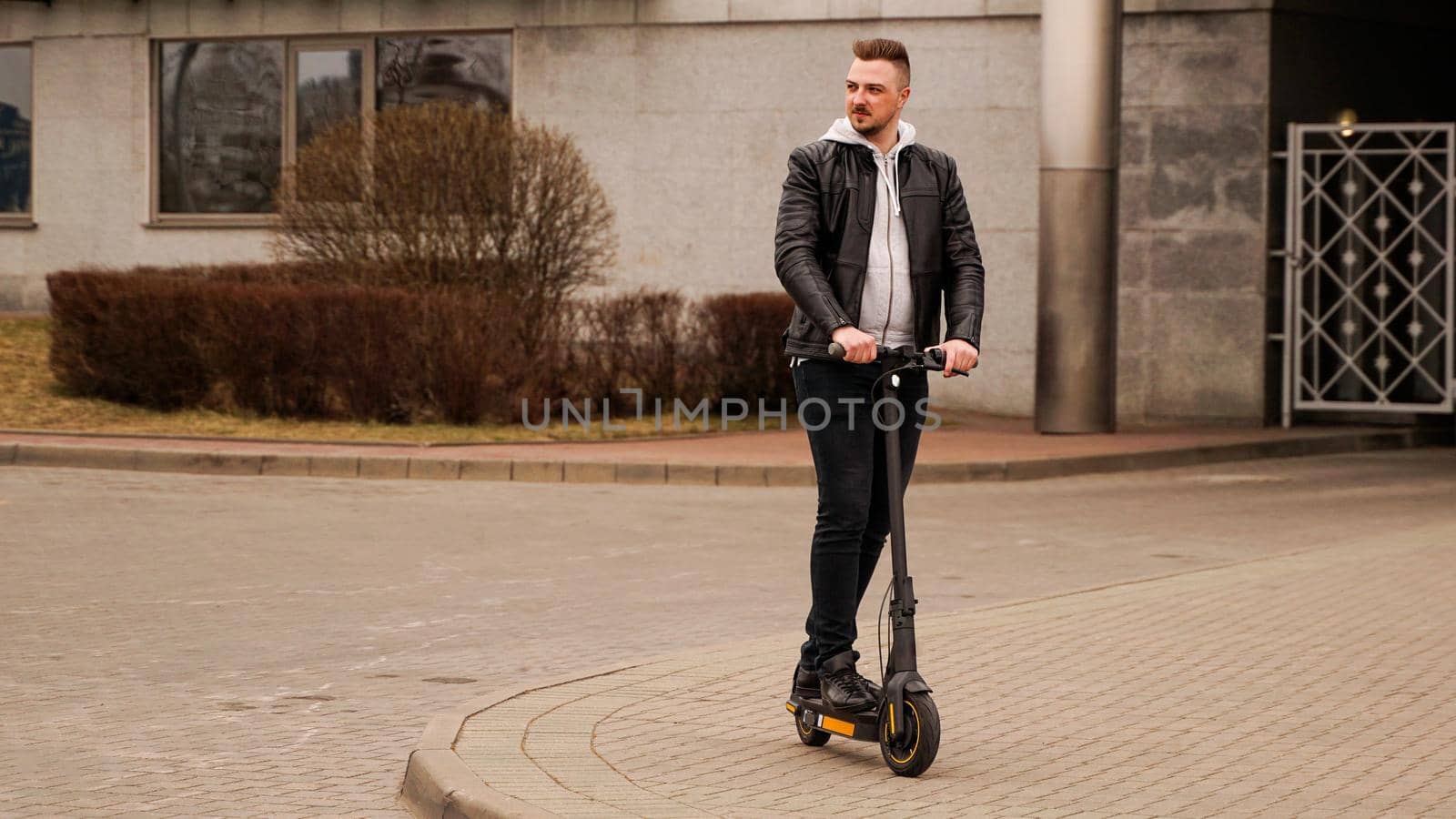 Tall man on an electric scooter against the backdrop of gray city buildings by natali_brill