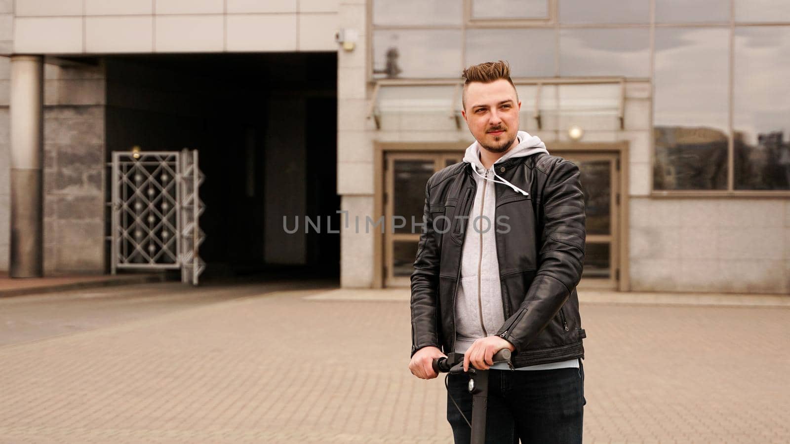 Tall man on an electric scooter against the backdrop of gray city buildings by natali_brill