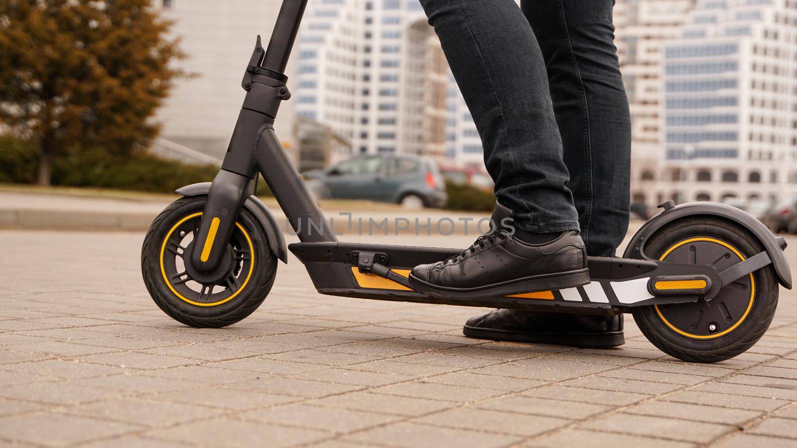 Close up of male feet standing on electric scooter on road at city street. Urban transportation. A man puts a kick scooter