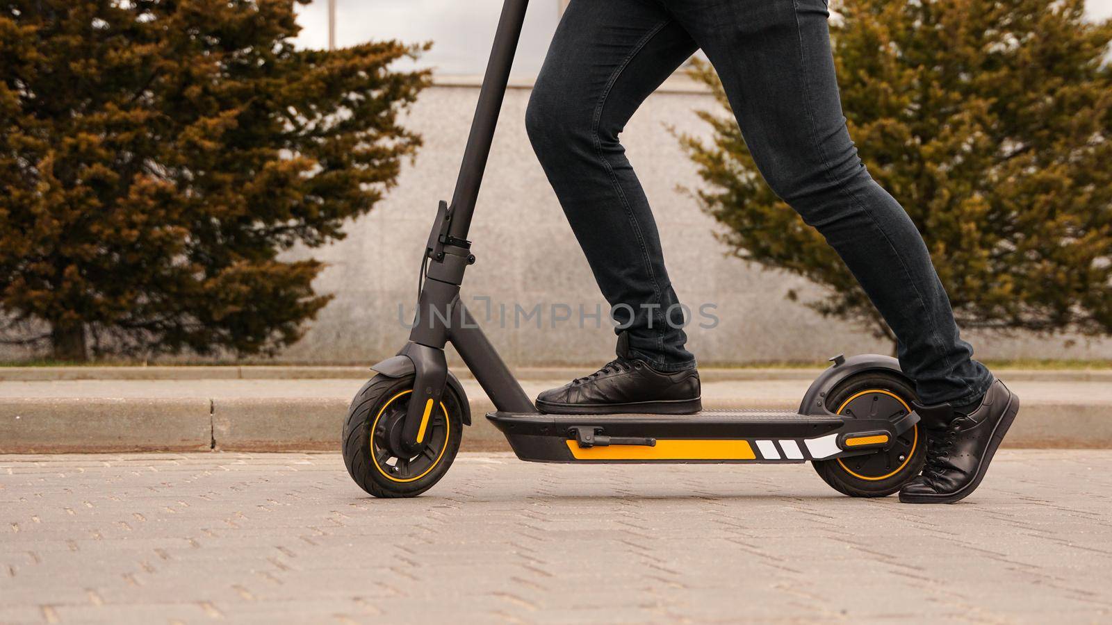 Cropped image of young man riding in the street on electric kick scooter. A man starts to ride a scooter