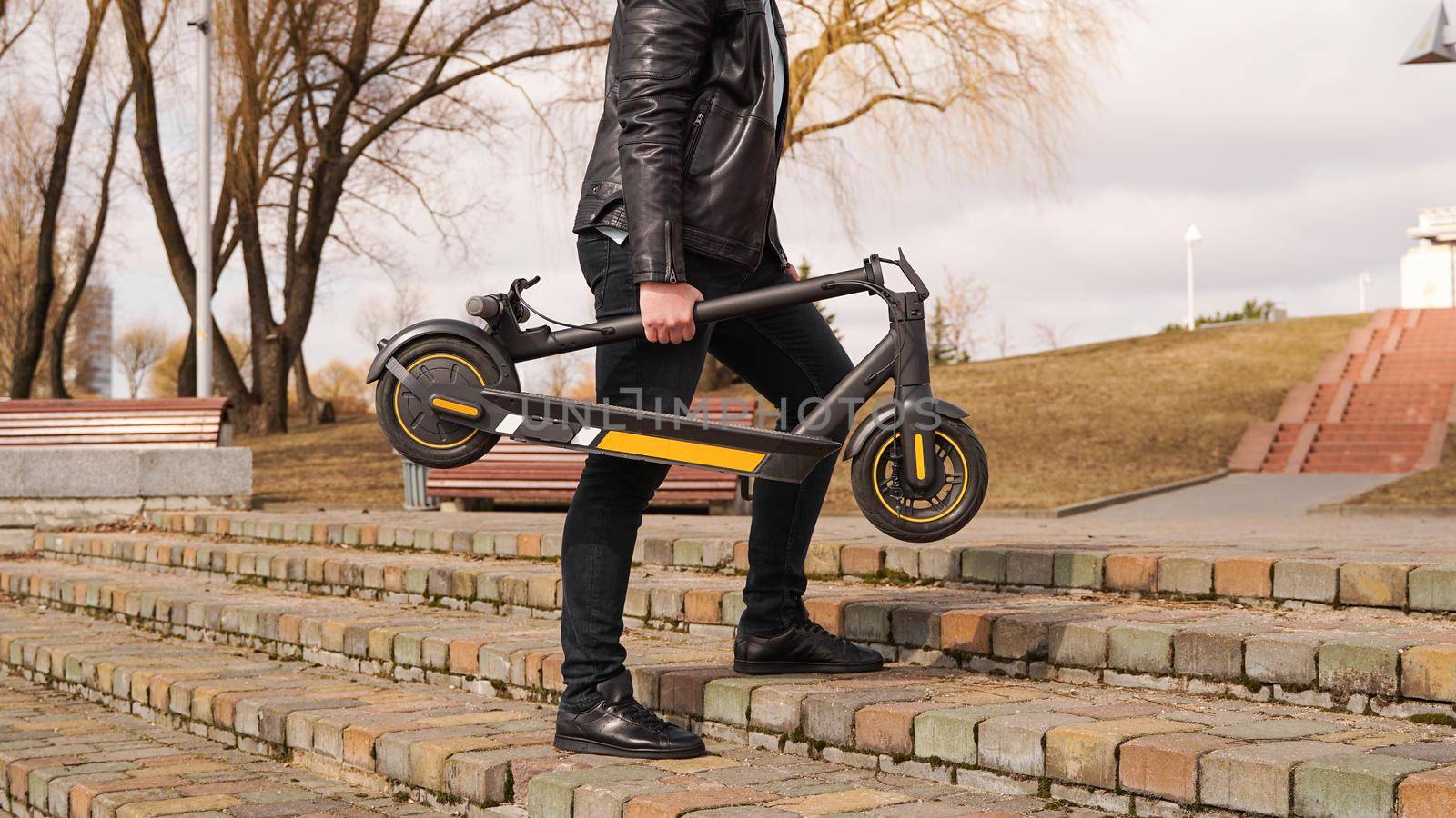 Close up of young men carries electrical kick scooter in hand, environment friendly transport