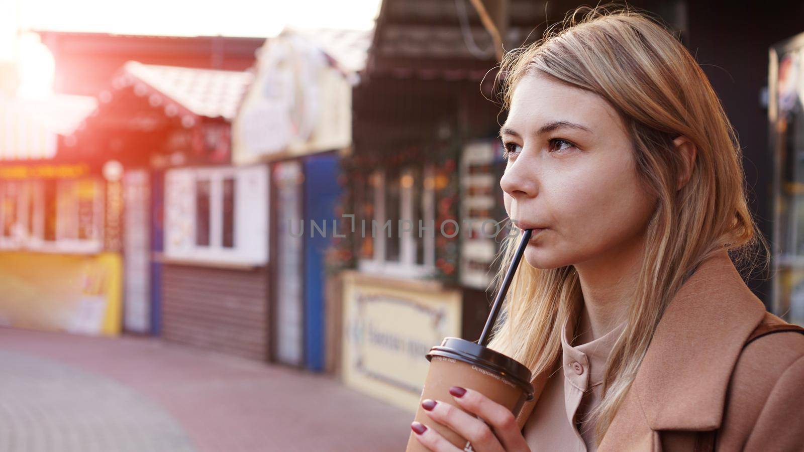 Young blonde with a cup of coffee. Woman at the food court. Lifestyle photo. Beautiful woman drinking coffee. Glare of the sun