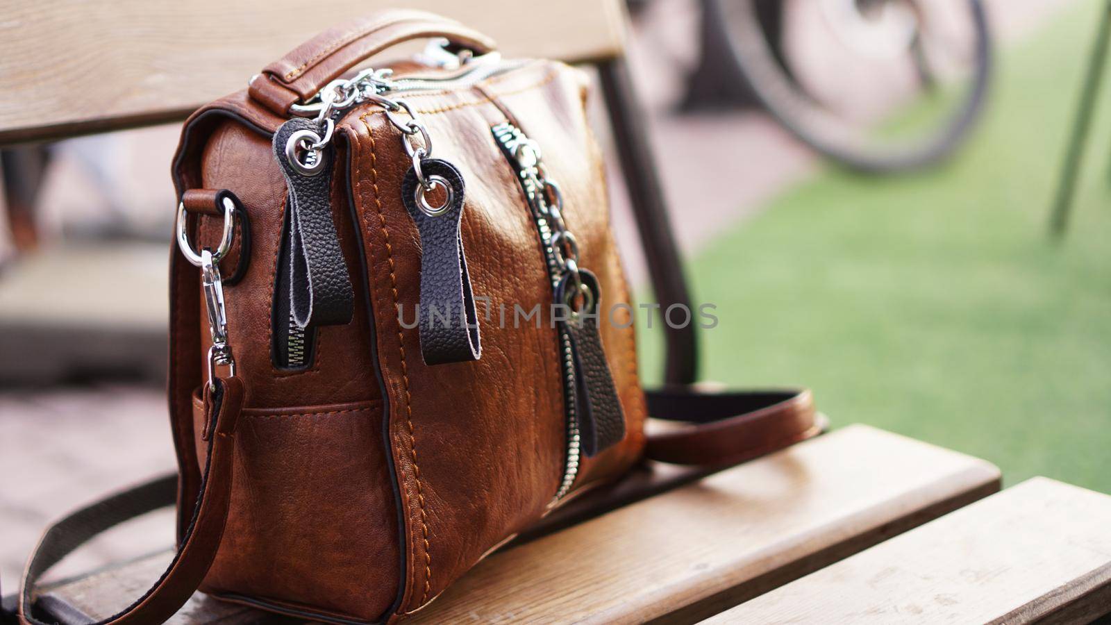 Brown leather bag outside. Blurred summer background. City walk or travel concept