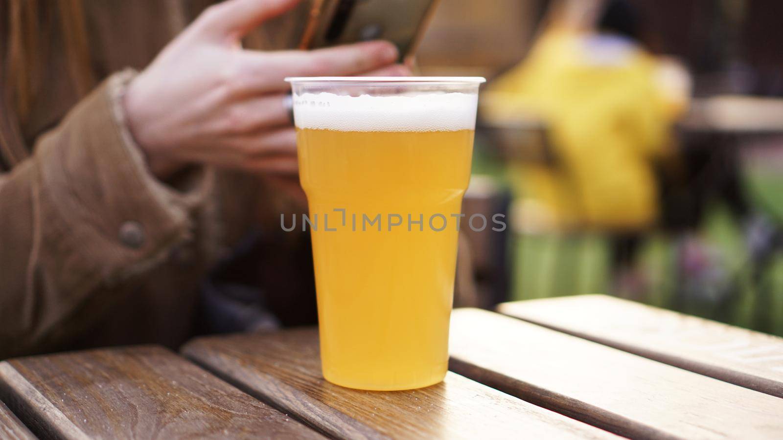 Light beer in a plastic glass. Girl drinking beer at the food court - blurred background