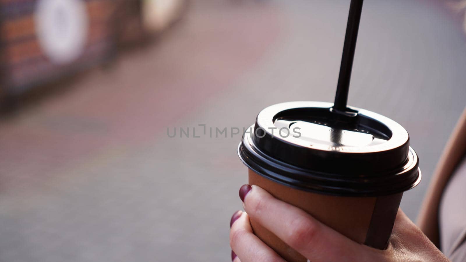 Woman's hand holding a cup of coffee outside against the backdrop of the city sidewalk