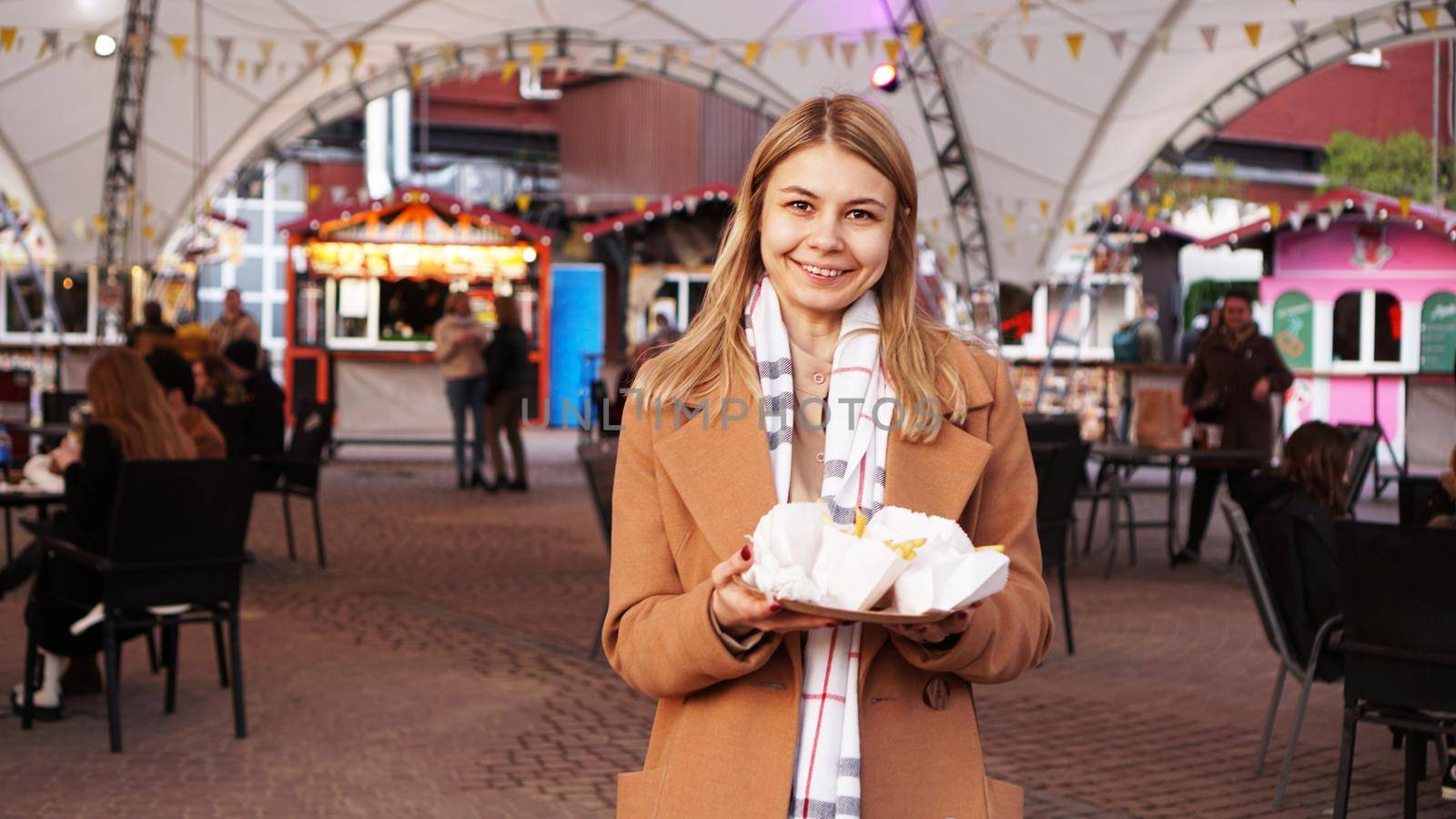 Woman at the food court with food trucks. The blonde has bought some street food and goes to her table. She smiles and looks at the camera