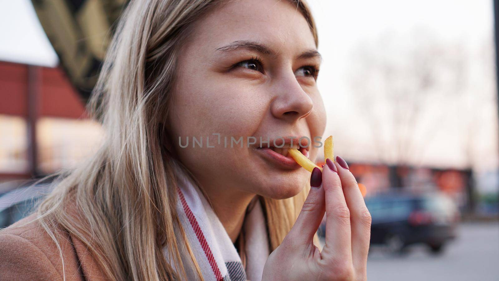 Young blonde eating French fries at the food court. Street food concept. by natali_brill