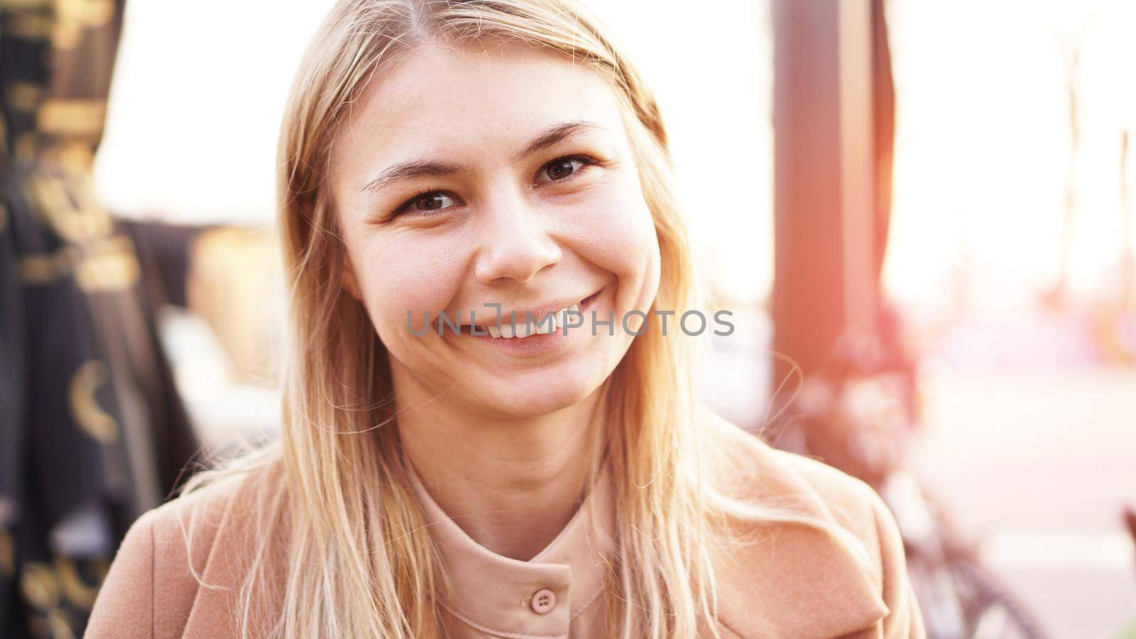 Portrait of a young woman in the city. City food court with street food. Portrait of a smiling blonde. Glare of the sun