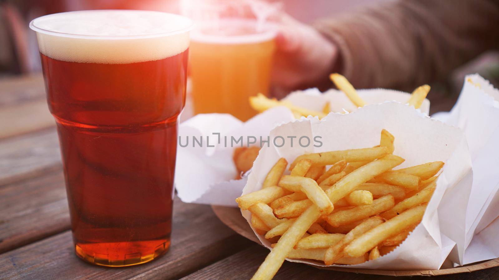 Girlfriends drink beer at the street food festival. Plastic glass of beer in hand. French fries, unhealthy food. Glare of the sun