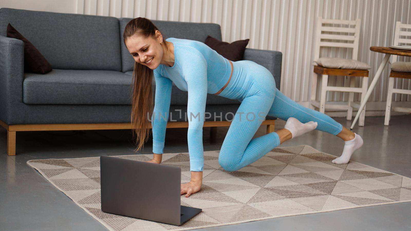 Beautiful young woman doing fitness exercise at home with her laptop by natali_brill