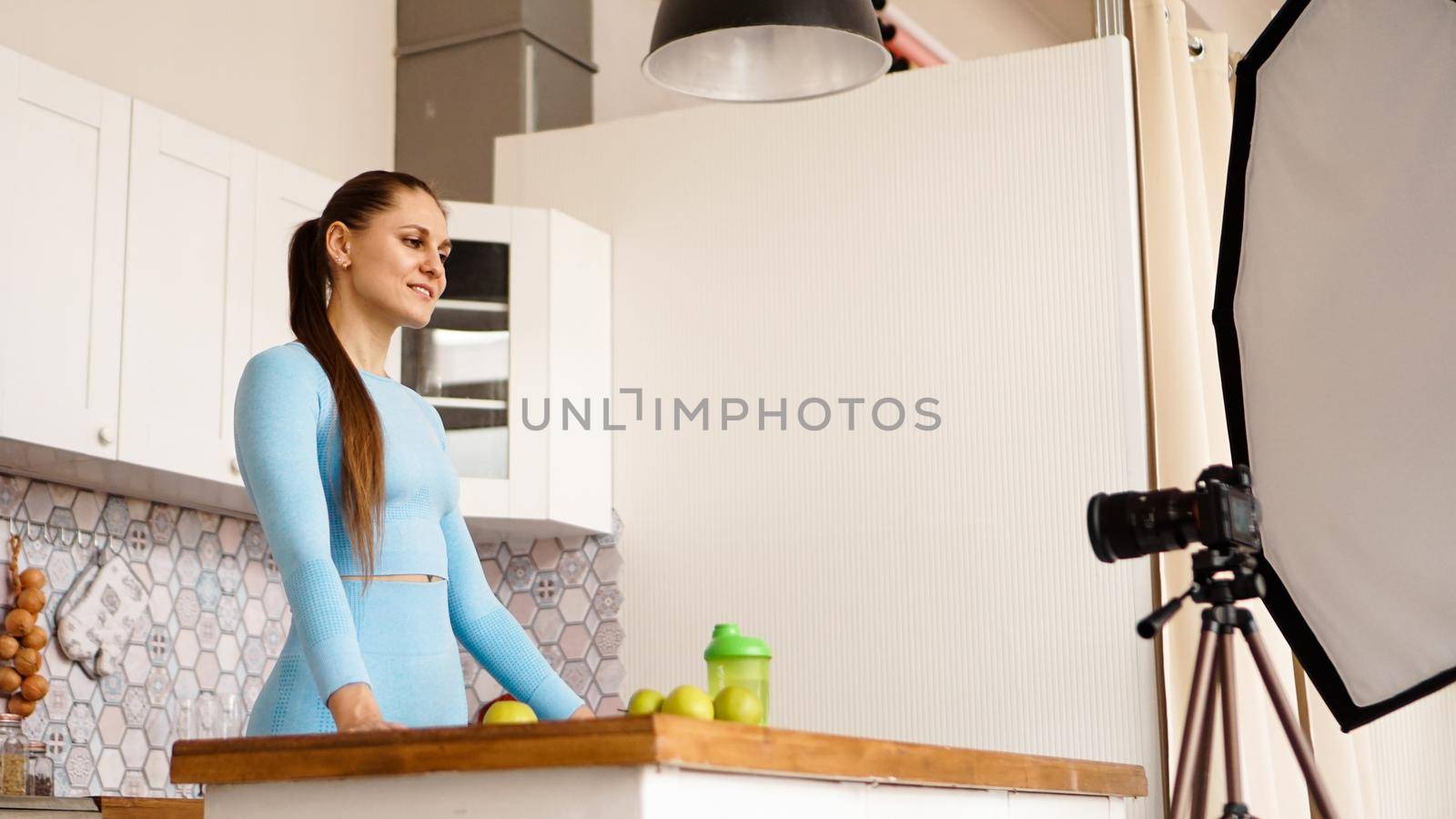 A woman in a tracksuit records a video blog about sports and healthy eating. Professional equipment in the photo studio with kitchen interior