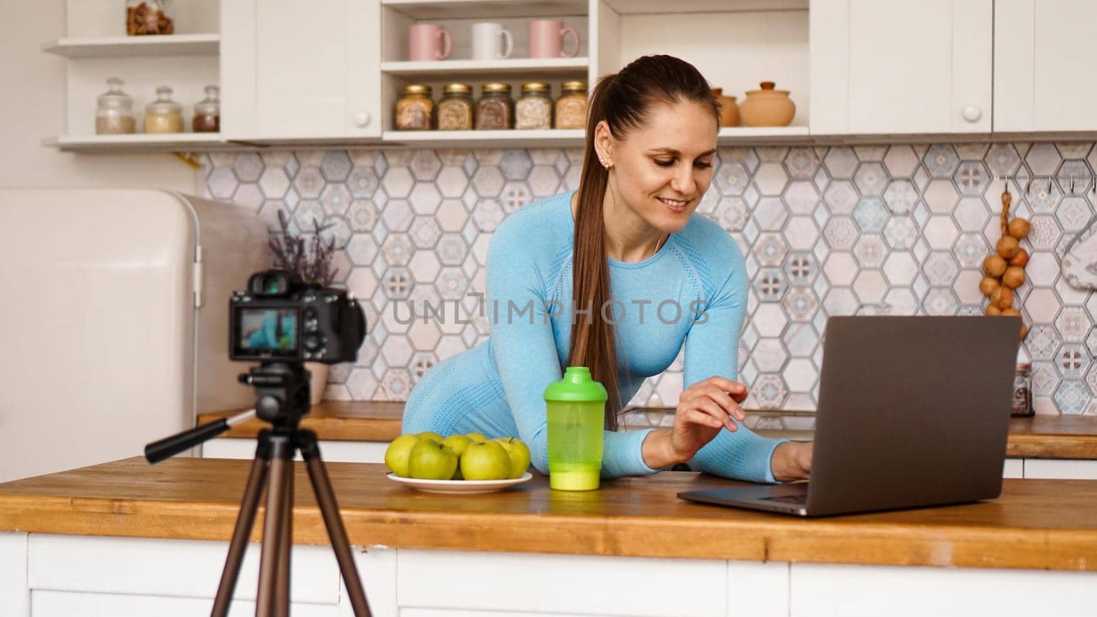 Young woman in kitchen with laptop smiling. Food blogger concept. A woman is recording a video about healthy eating. Camera on a tripod.