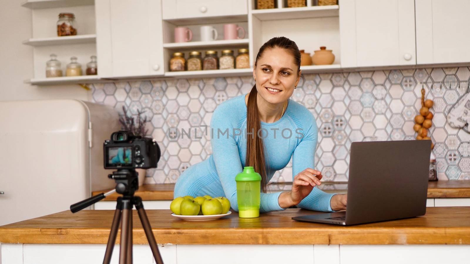 Young woman in kitchen with laptop smiling. Food blogger concept. A woman is recording a video about healthy eating. Camera on a tripod.