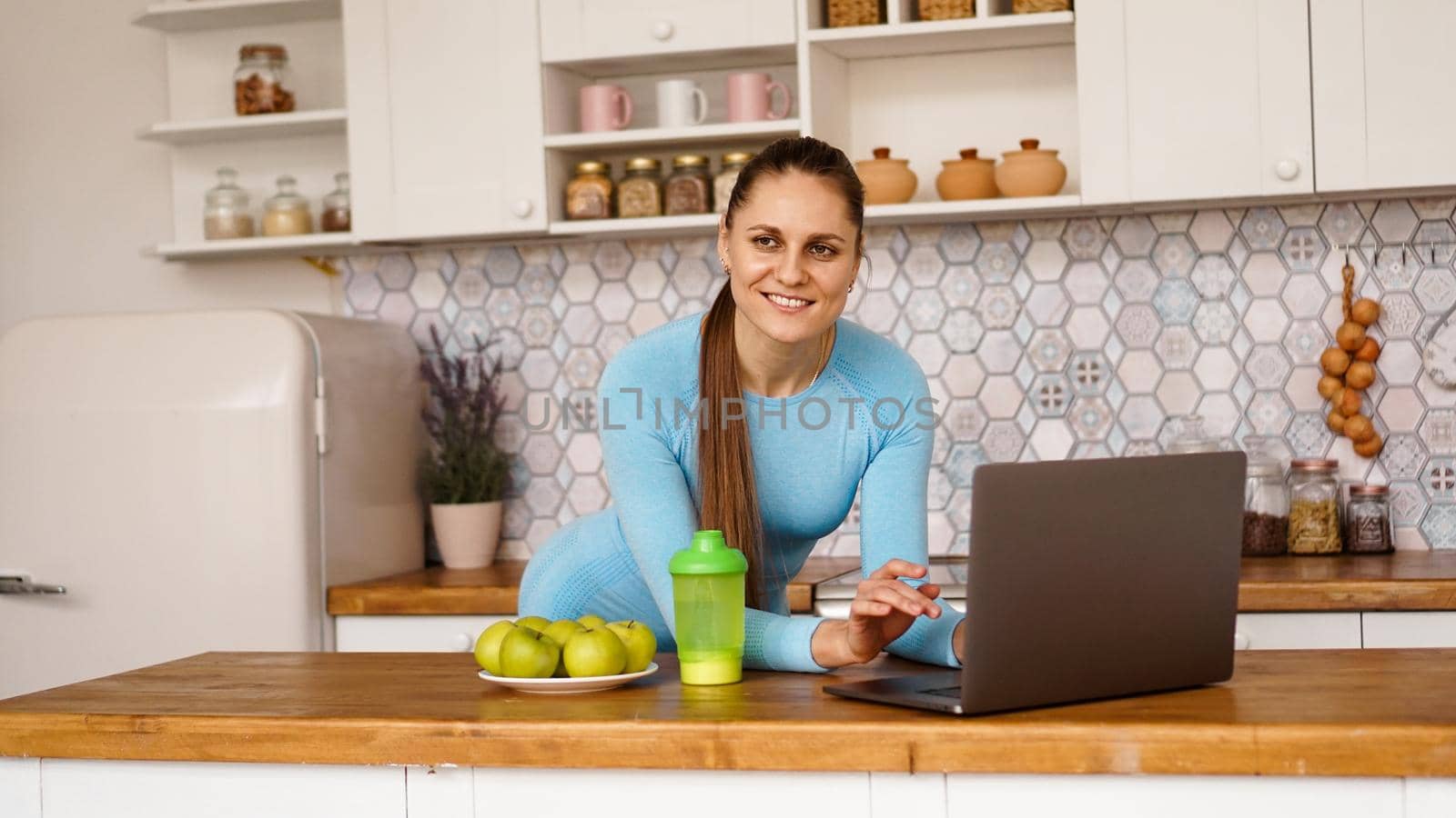 Smiling woman using computer in modern kitchen. Healthy lifestyle concept by natali_brill