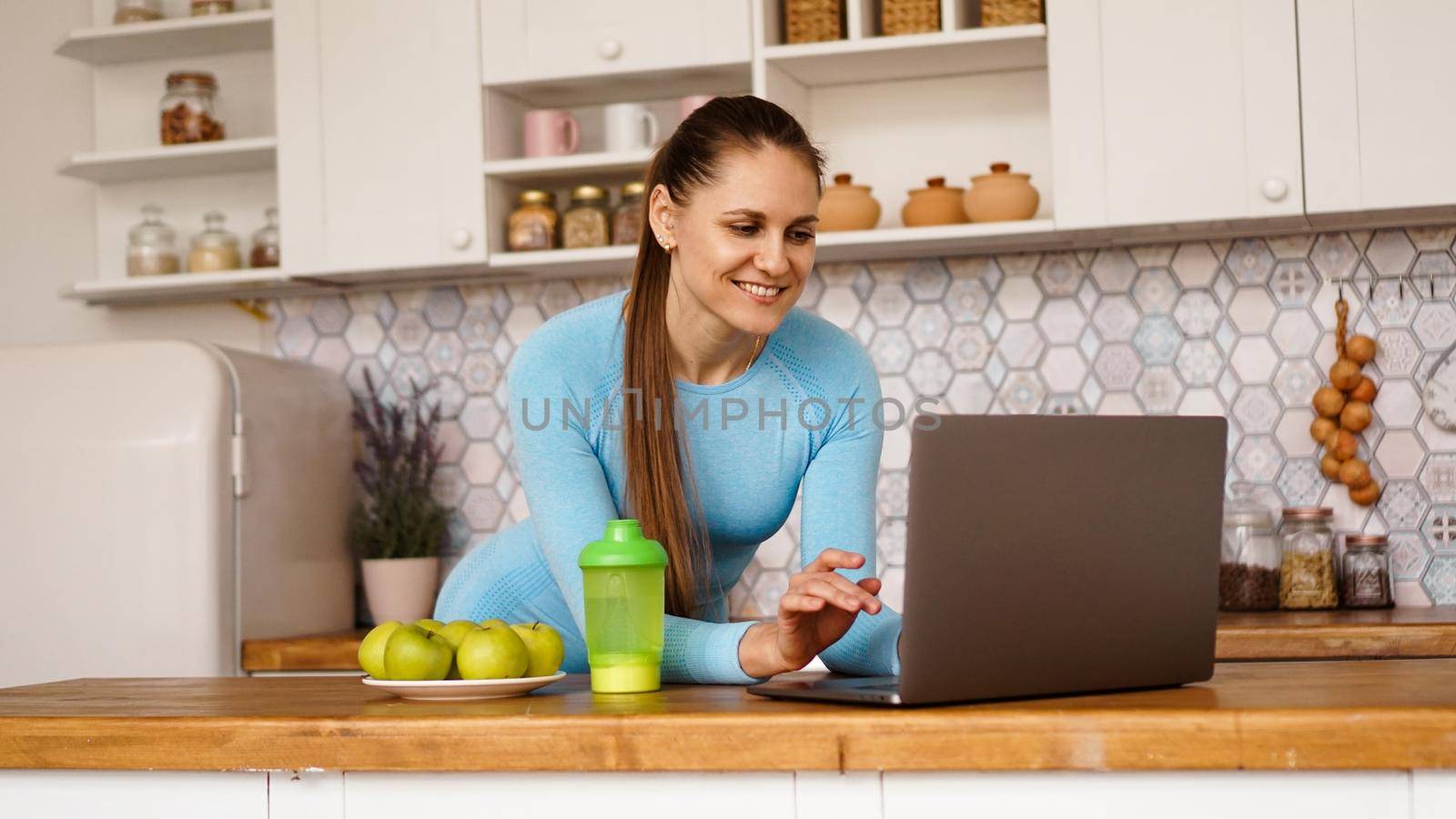 Smiling woman using computer in modern kitchen. Healthy lifestyle concept by natali_brill