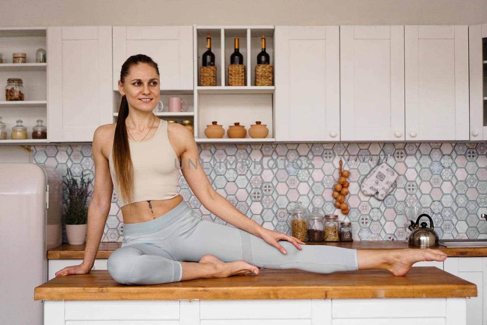 Athletic woman in sportswear posing on the table top of a light modern kitchen. The concept of beauty, health, proper nutrition.