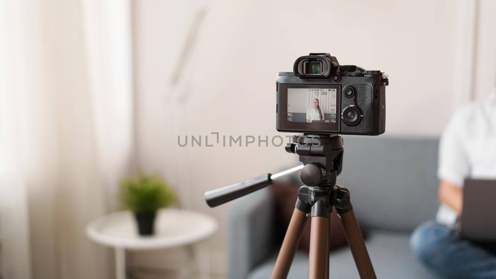 Woman blogger recording video indoors, selective focus on camera display. Space for text