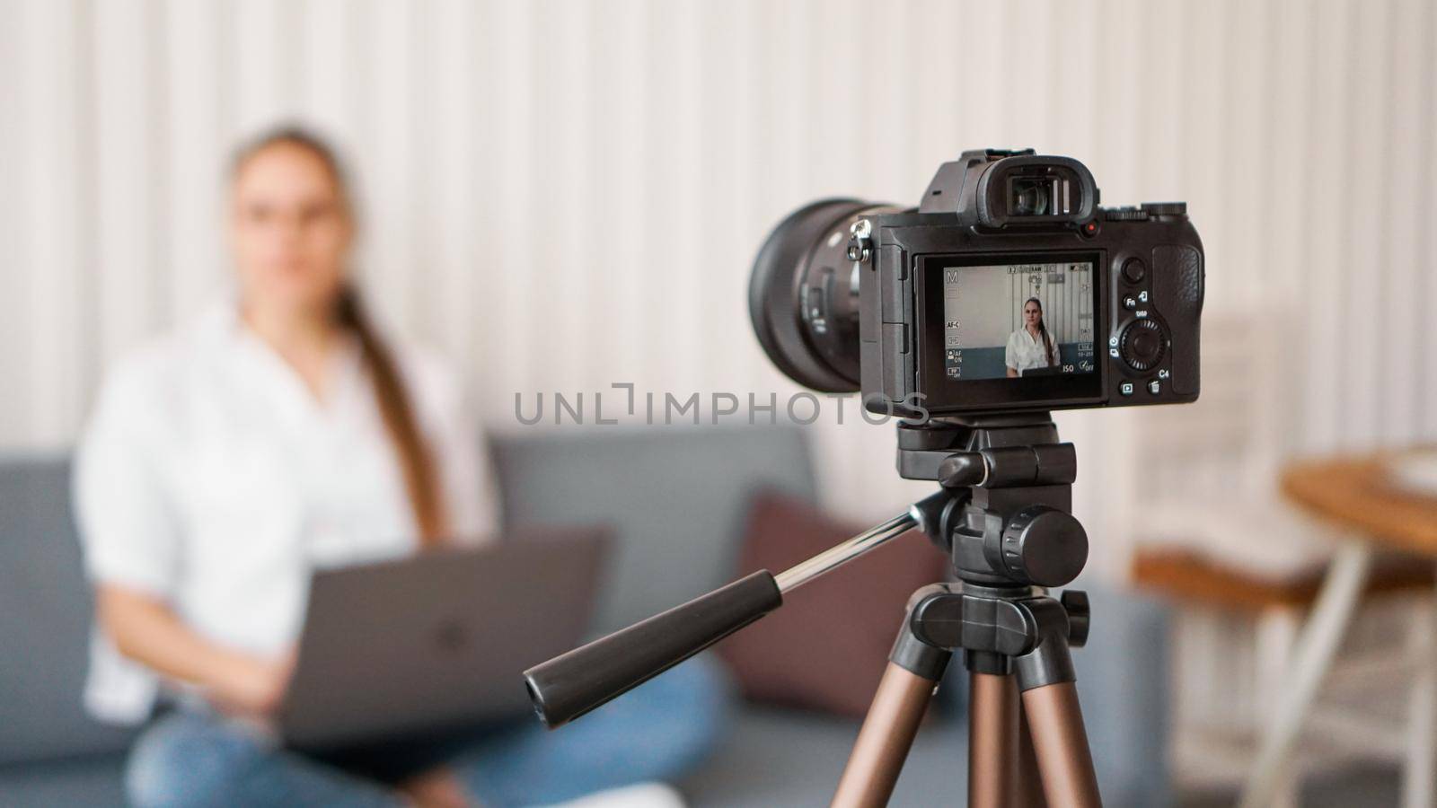 Woman blogger recording video indoors, selective focus on camera display. Space for text