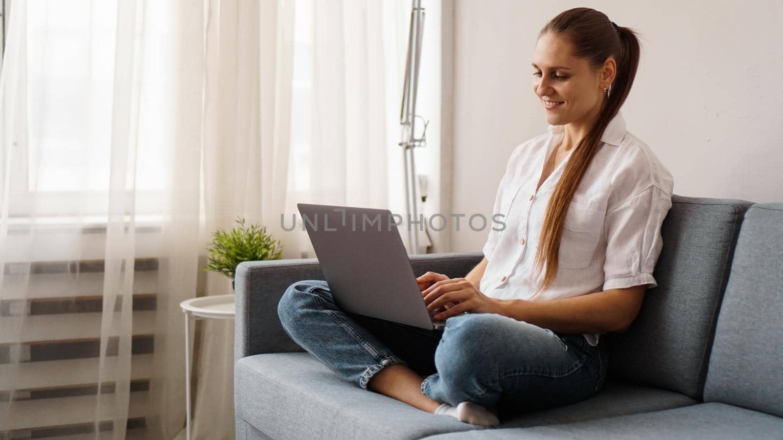 Smiling happy woman sitting on the sofa and using laptop. The concept of remote work or study during quarantine.