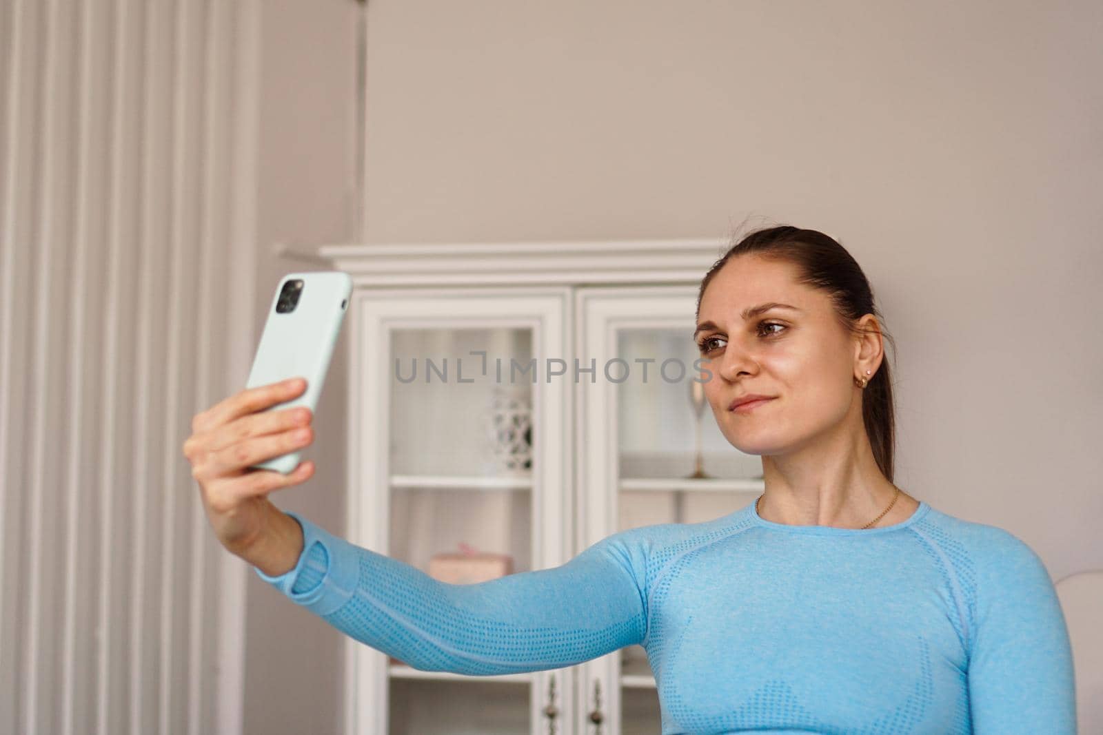 Indoor shot of beautiful woman wearing sports clothes, taking selfie using mobile phone after exercising.