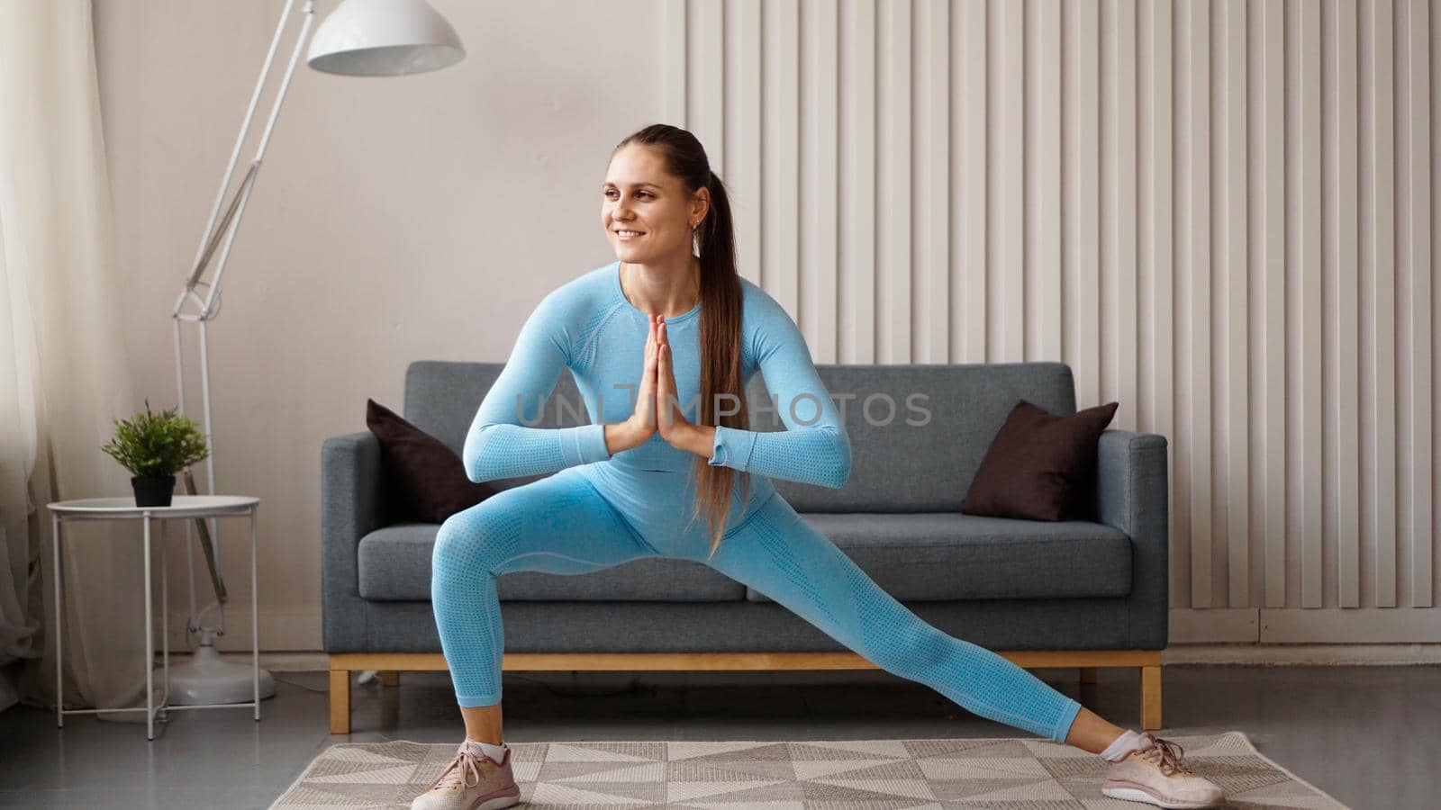 Young determined confident slim woman doing exercises at home. Fitness trainer trains at home during quarantine. Light modern interior