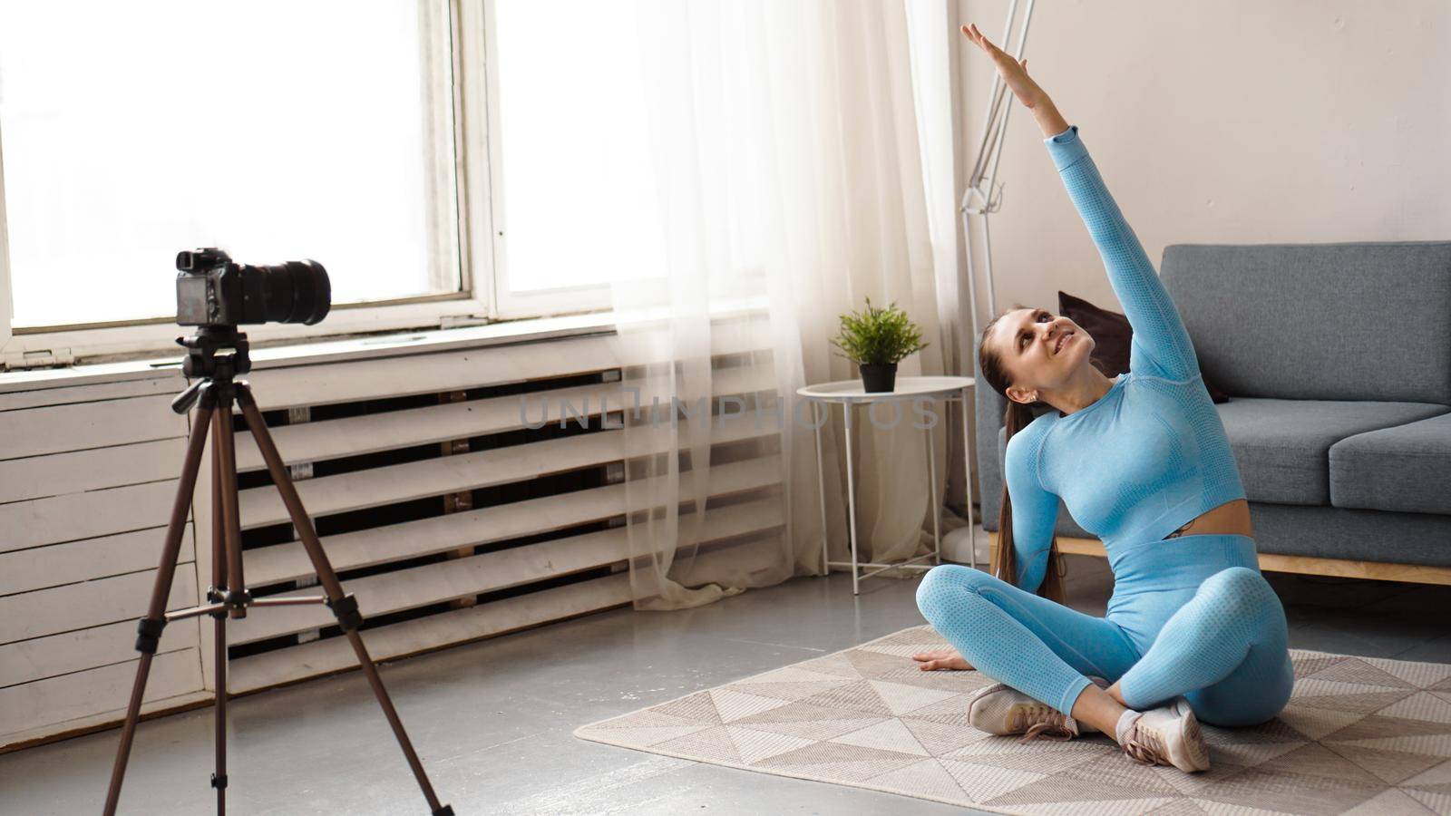 Athletic woman blogger in sportswear shoots video on camera at home in the living room. Sport and recreation concept. Healthy lifestyle.
