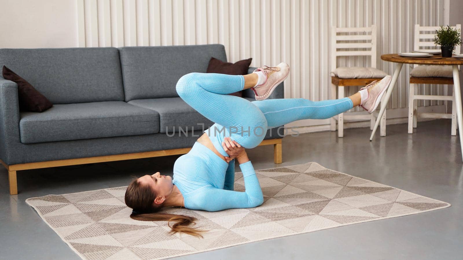 Young determined confident slim woman doing exercises at home. Fitness trainer trains at home during quarantine. Light modern interior