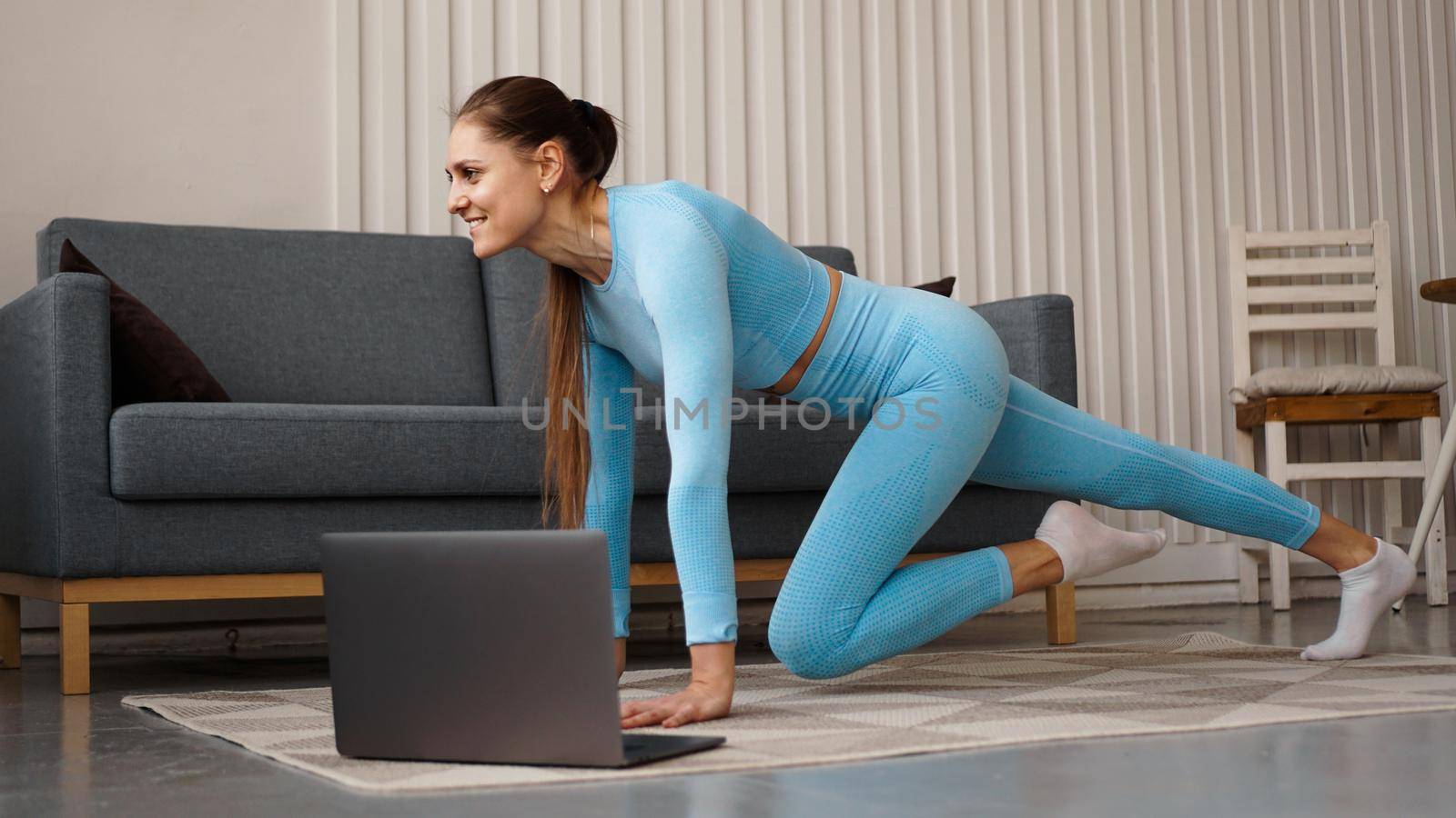 Beautiful young woman doing fitness exercise at home with her laptop by natali_brill