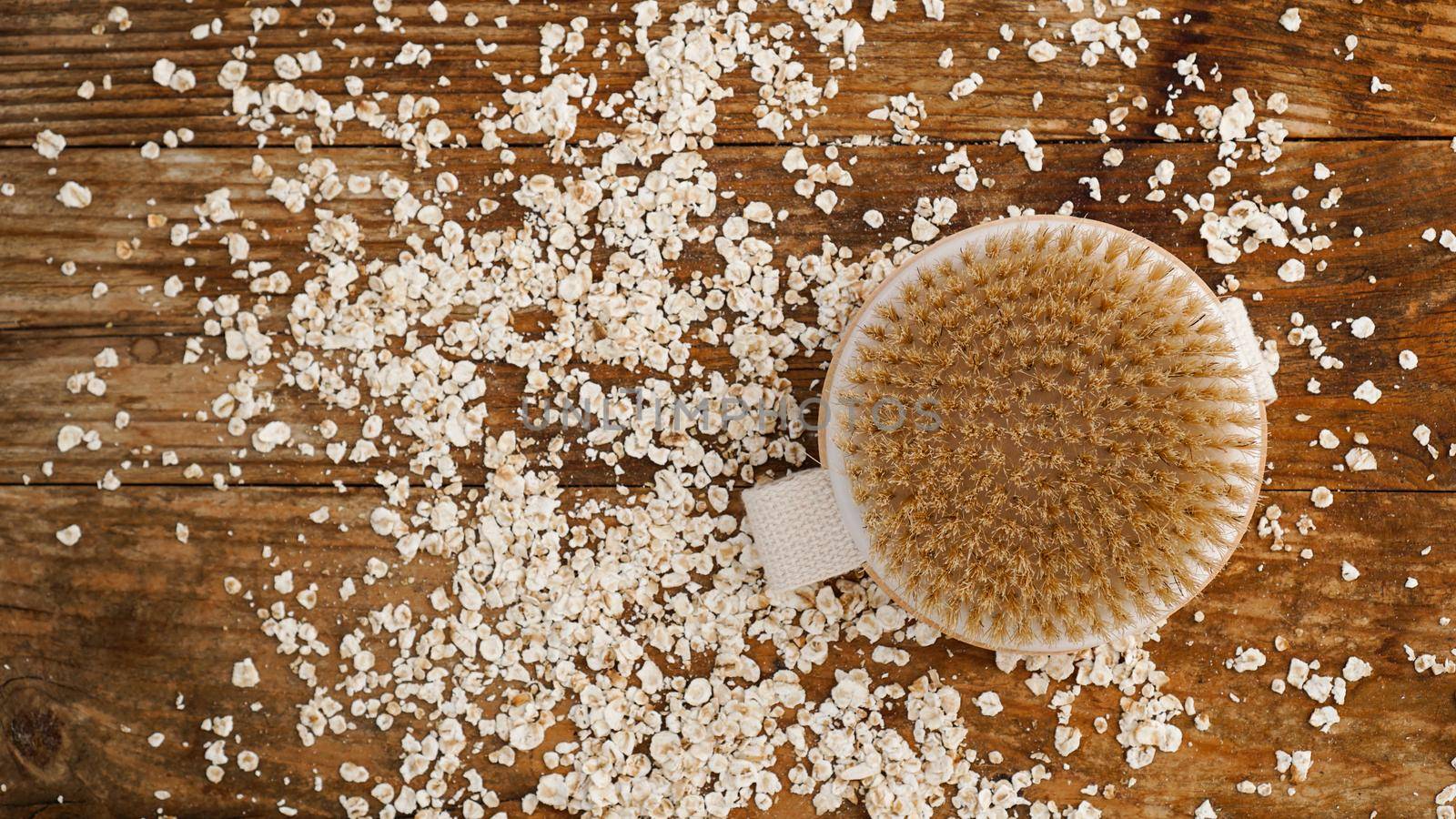 Wooden round massage brush on a wooden background. Scattered oatmeal. The concept of cosmetics for body from natural ingredients