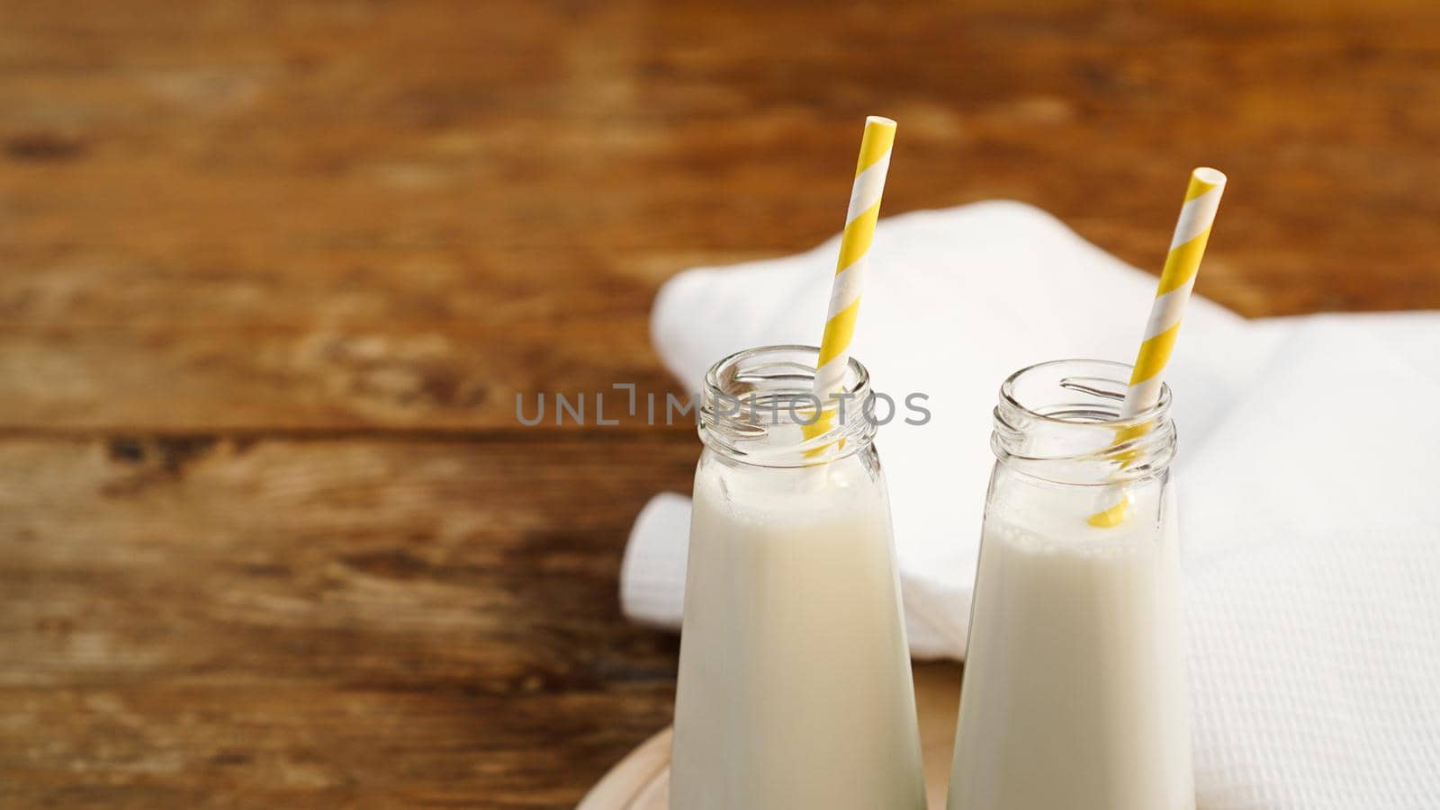 Two bottles of organic rustic milk on wooden table with yellow paper straws. Copy space