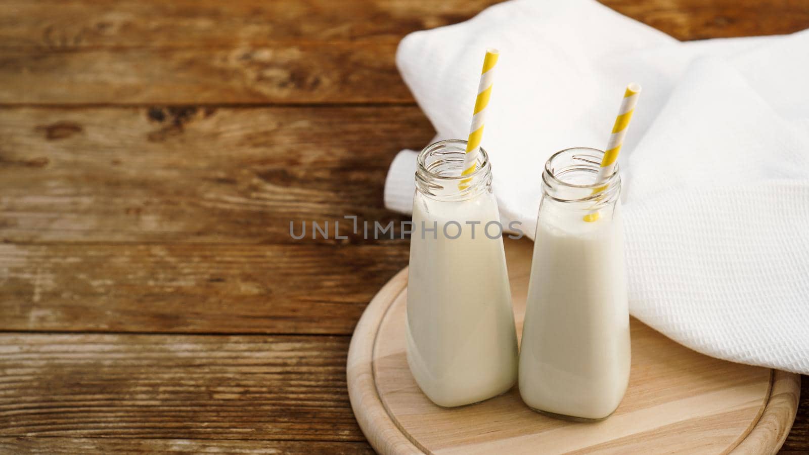 Two bottles of organic rustic milk on wooden table with yellow paper straws. Copy space