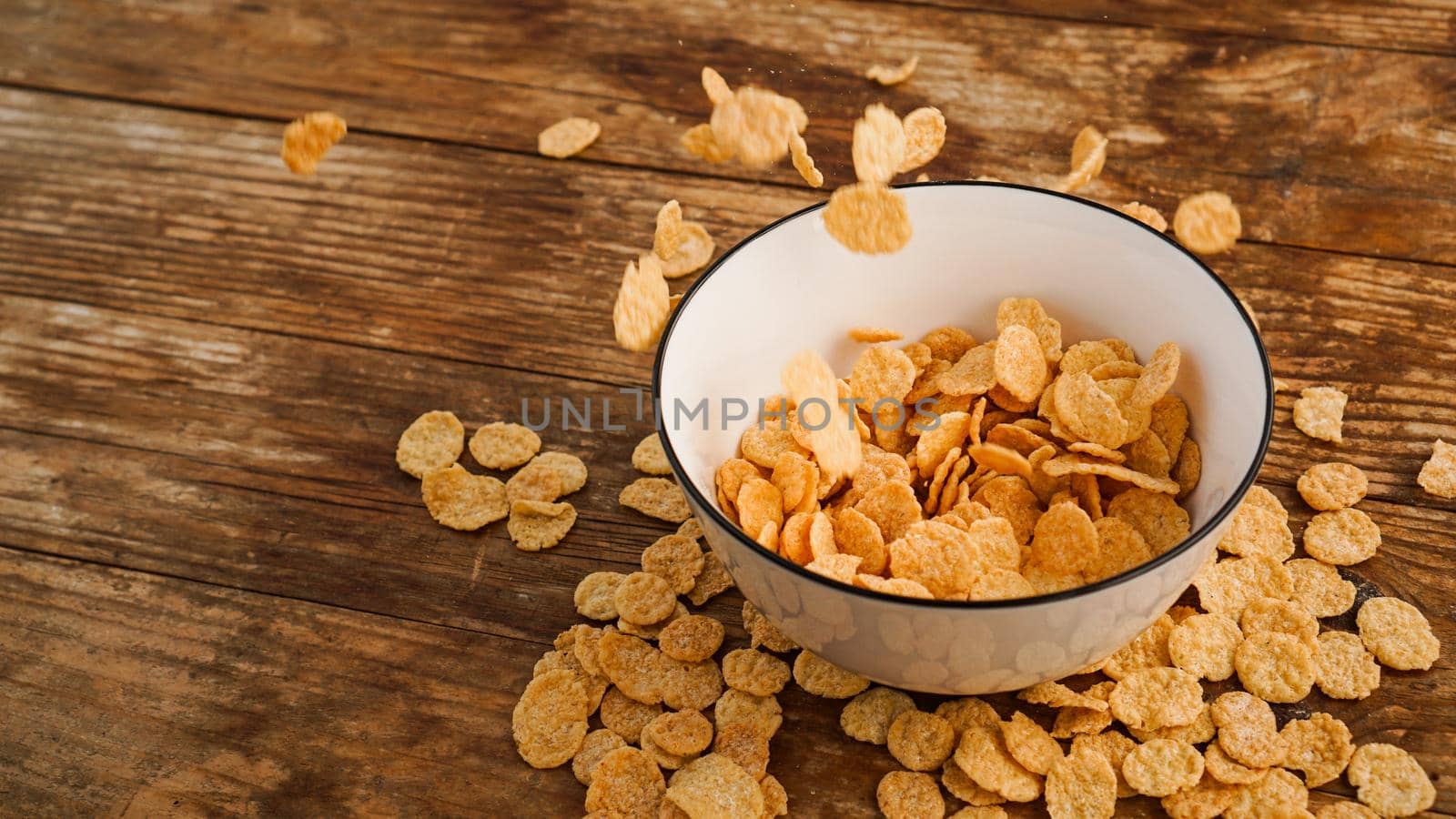 Cereals falling in a white bowl on a wooden table. Bright photo. Healthy quick breakfast