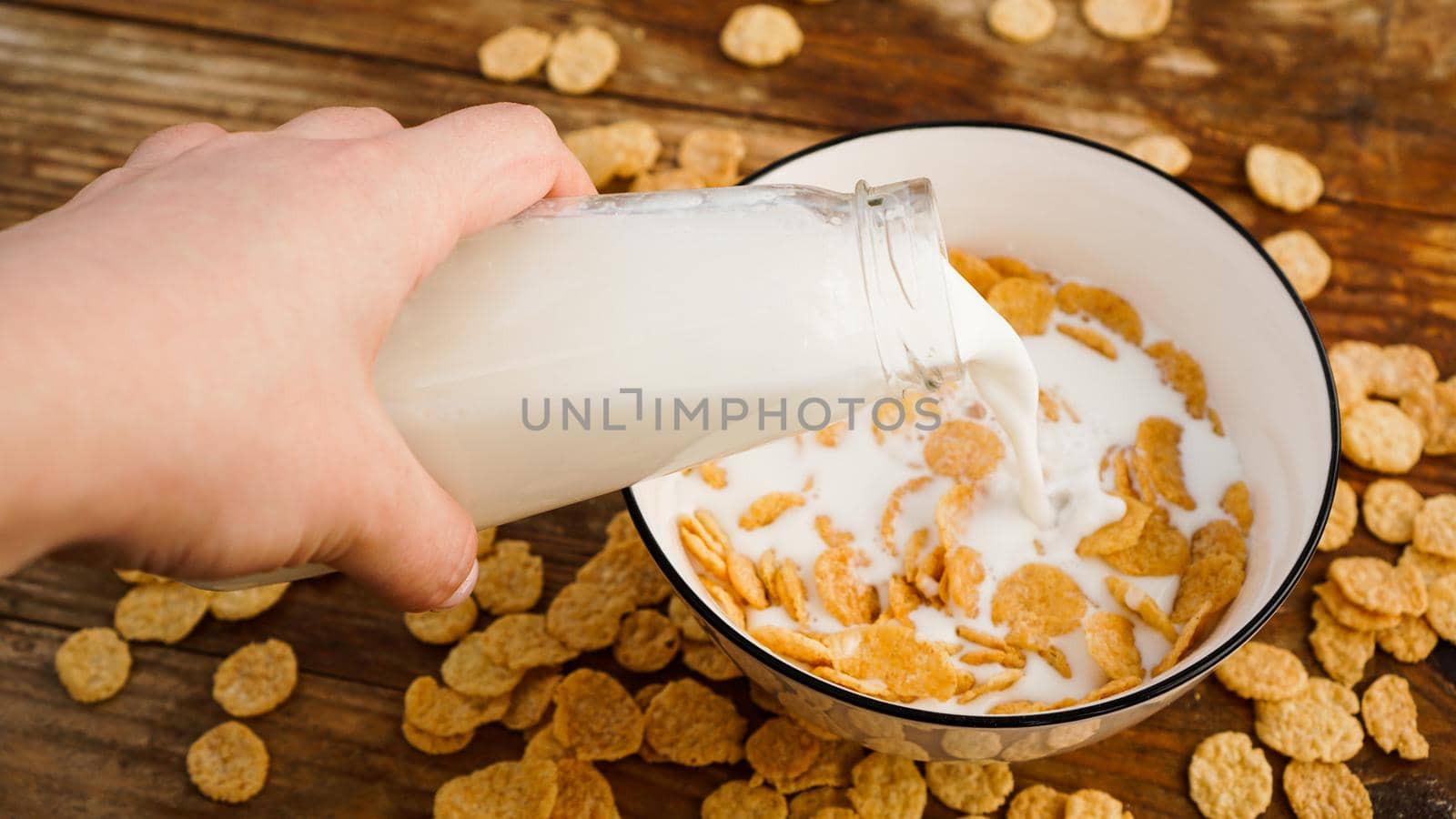 Healthy eating background. Pouring in fresh milk into bowl of cornflakes. Wood background