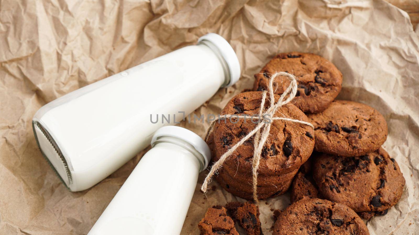 Cookies with chocolate drops on craft paper and bottles of milk. Natural handmade organic snakes for healthy breakfast