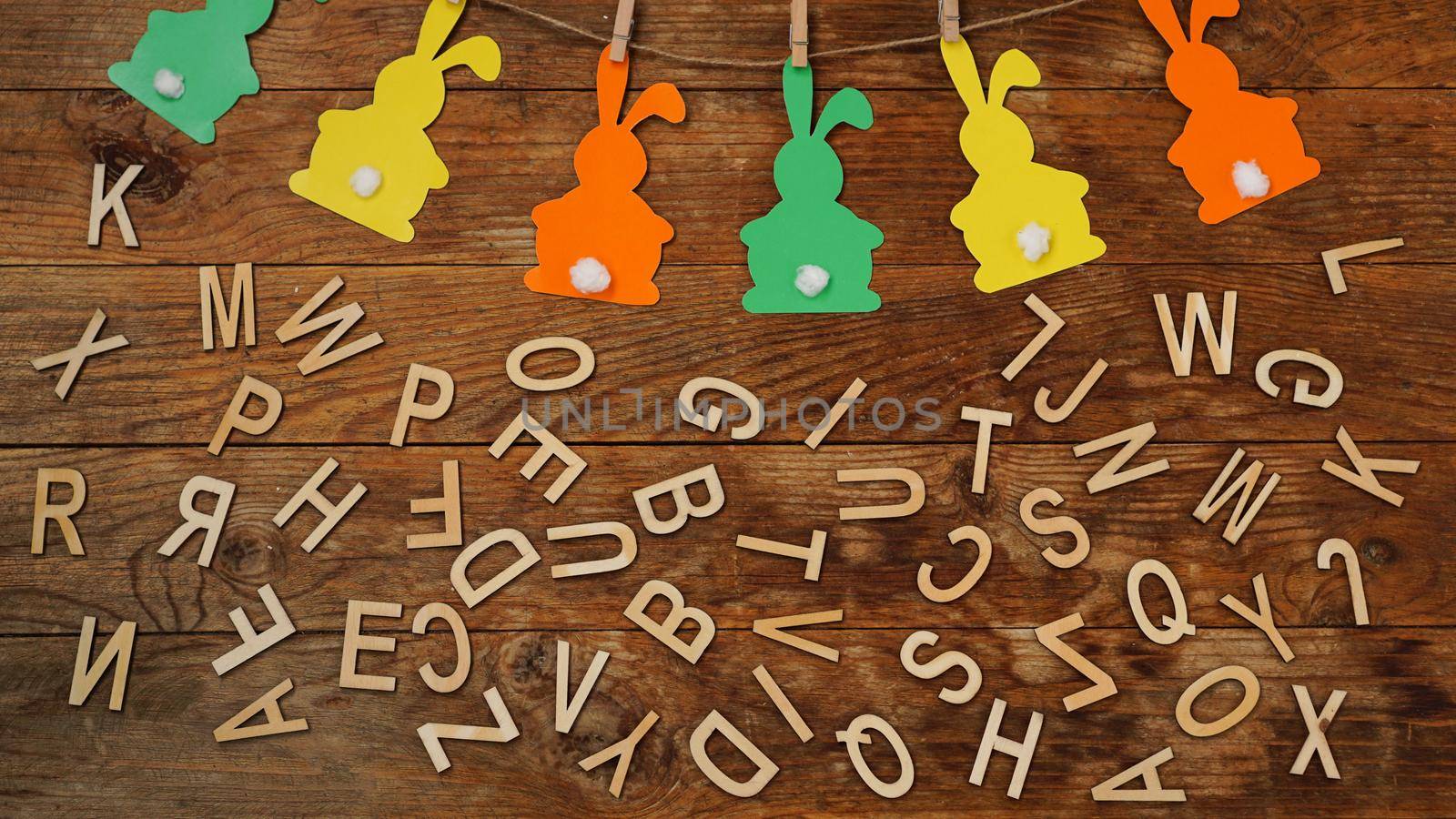 Easter background. Garland of paper rabbits and letters on wooden background. The letters of the English alphabet. Bunny background.