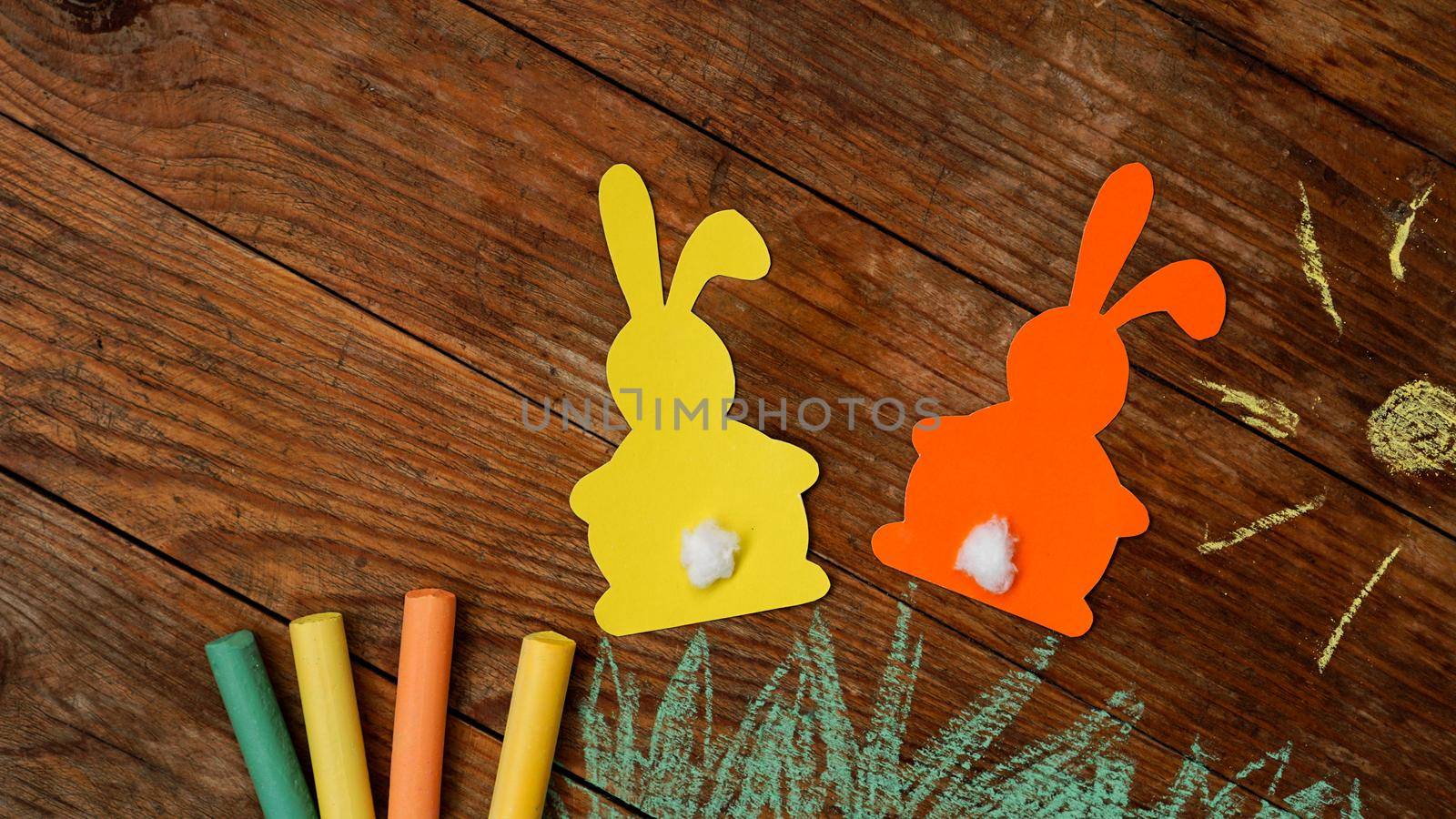 Two Easter bunnies made of paper. Drawn with colored chalk grass and sun by natali_brill