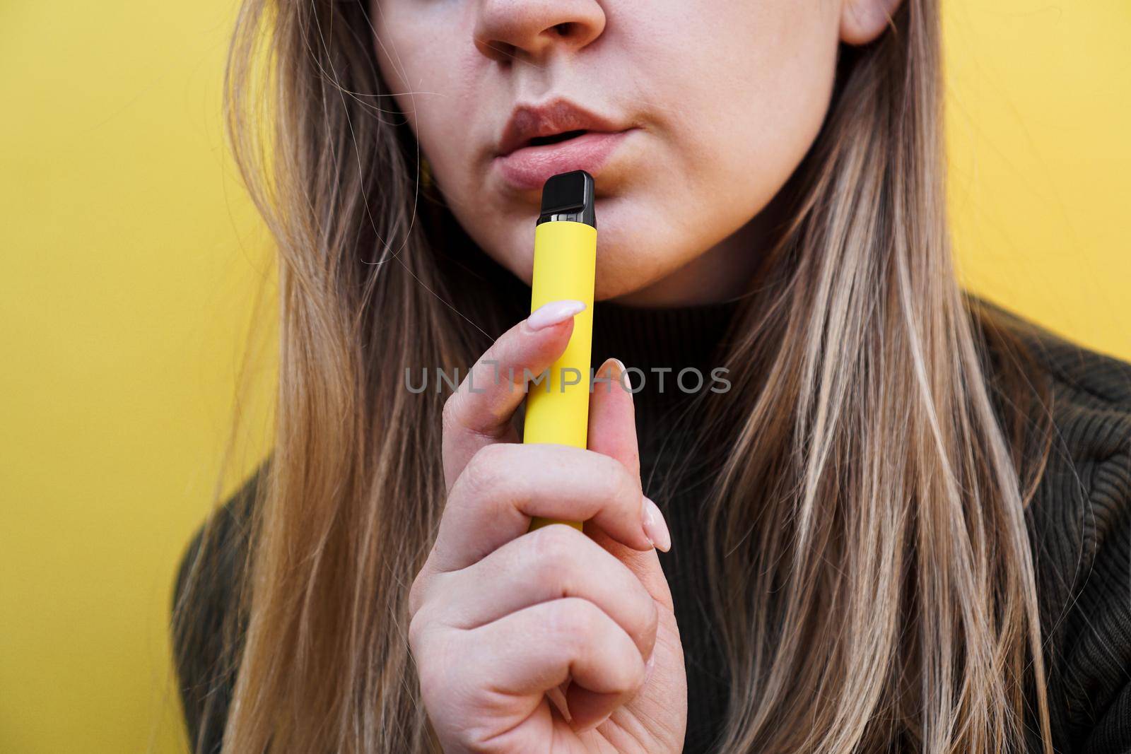 A young girl smokes disposable electronic cigarette. Bright yellow background by natali_brill