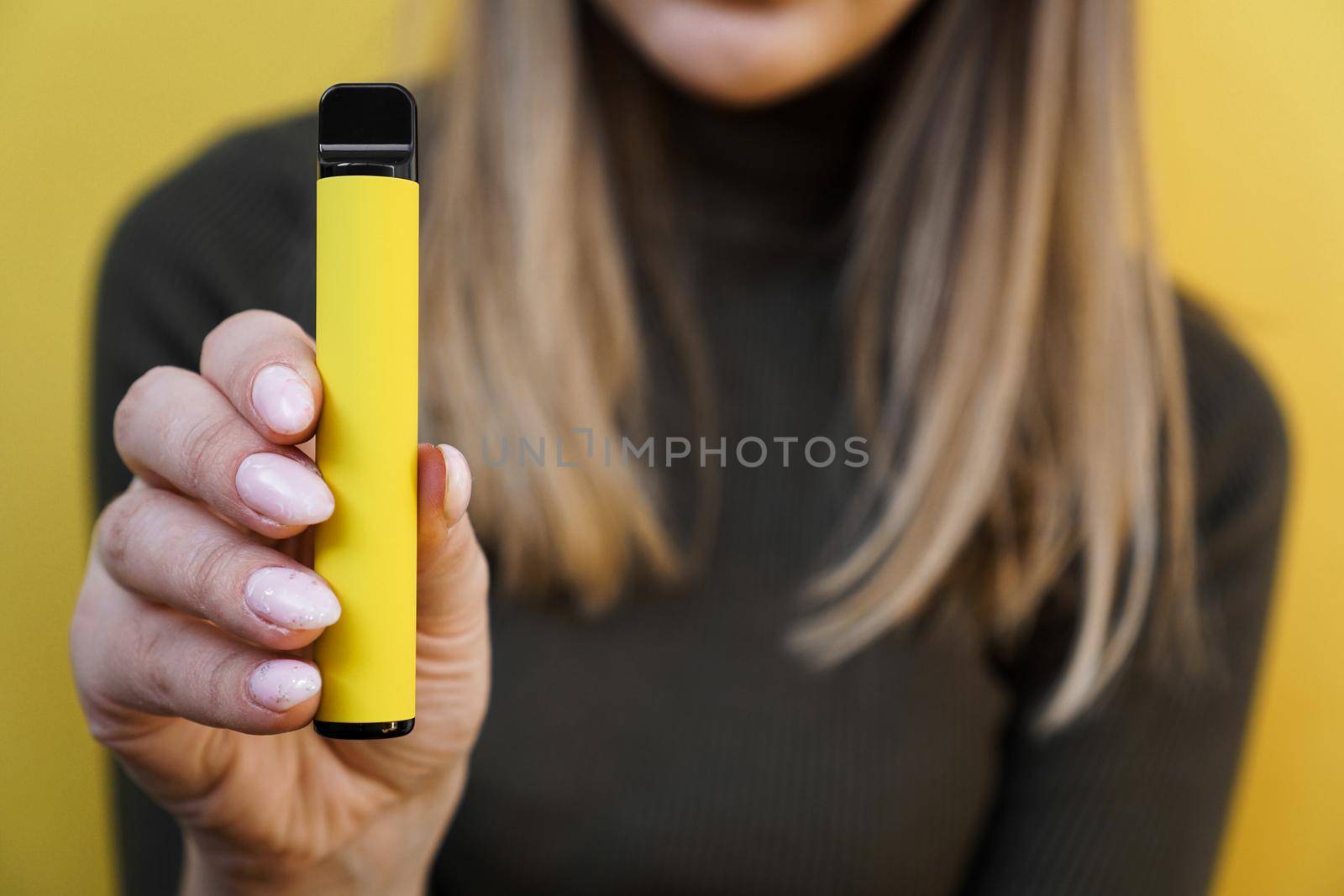 Yellow disposable electronic cigarette in a female hand. Bright yellow background. Melon, pineapple or lemon flavored vape