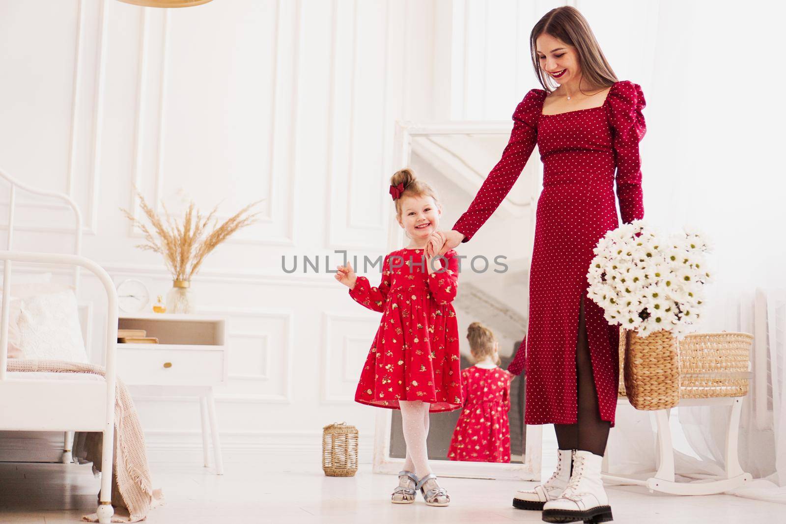 Mom and little daughter in red dresses in a bright bedroom by natali_brill