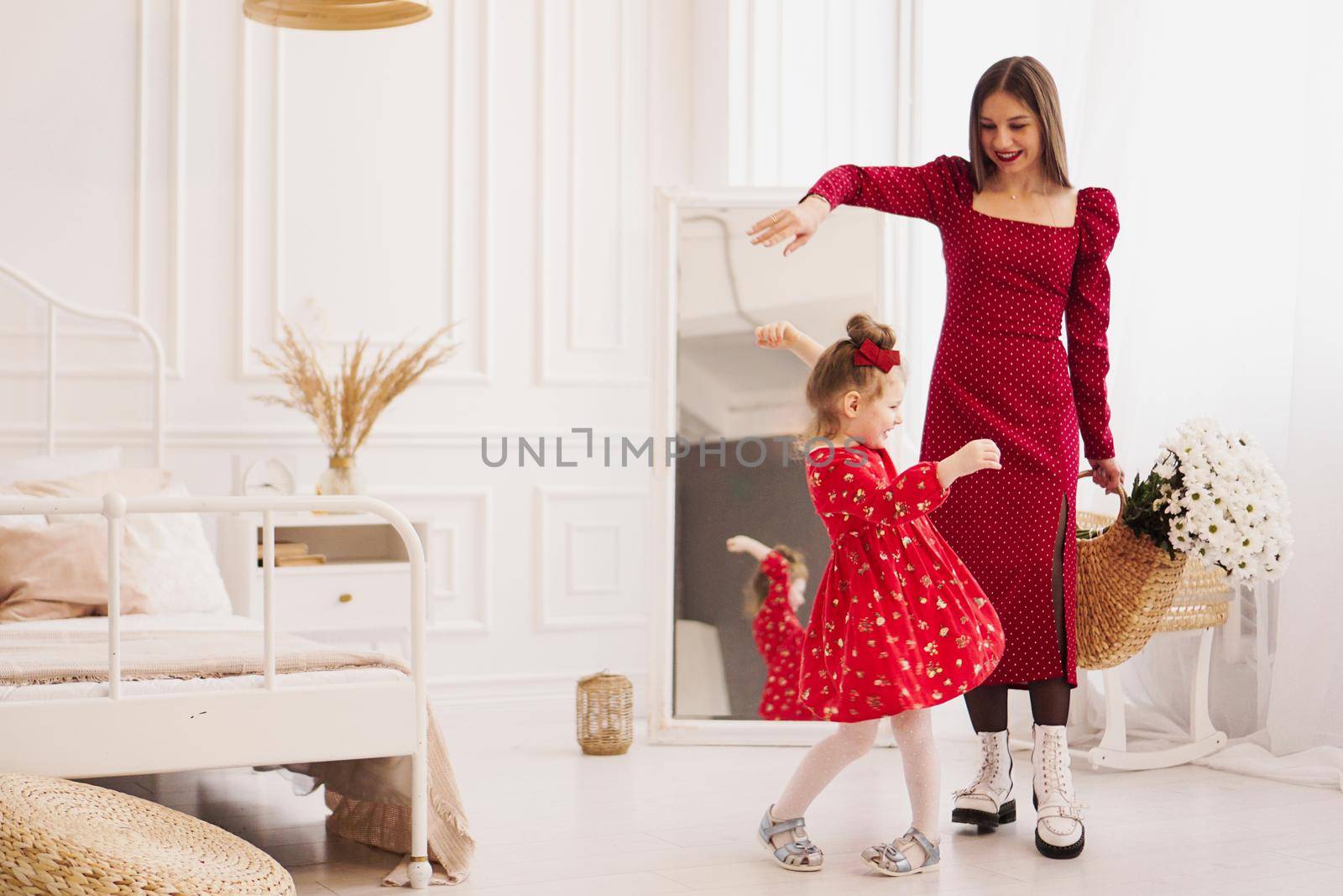 Mom and little daughter in red dresses in a bright bedroom in a Scandinavian style. Happy family. Mom holds a bouquet of daisies - spring photo