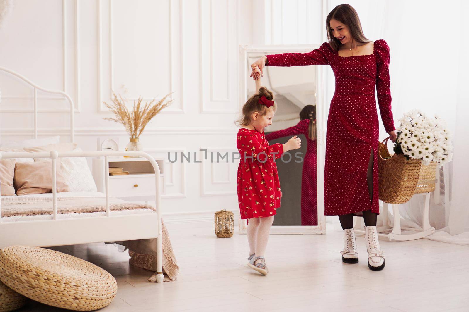 Mom and little daughter in red dresses in a bright bedroom by natali_brill