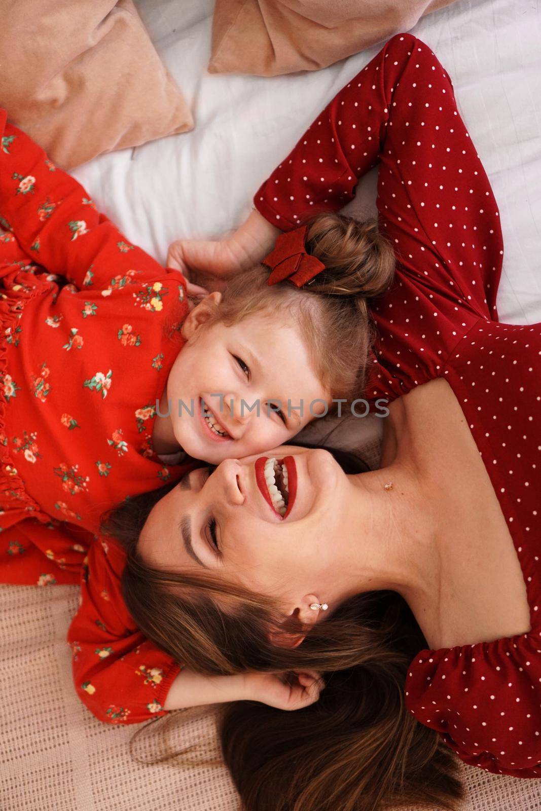 Mom and her little daughter lie on the bed facing each other. They are happy by natali_brill